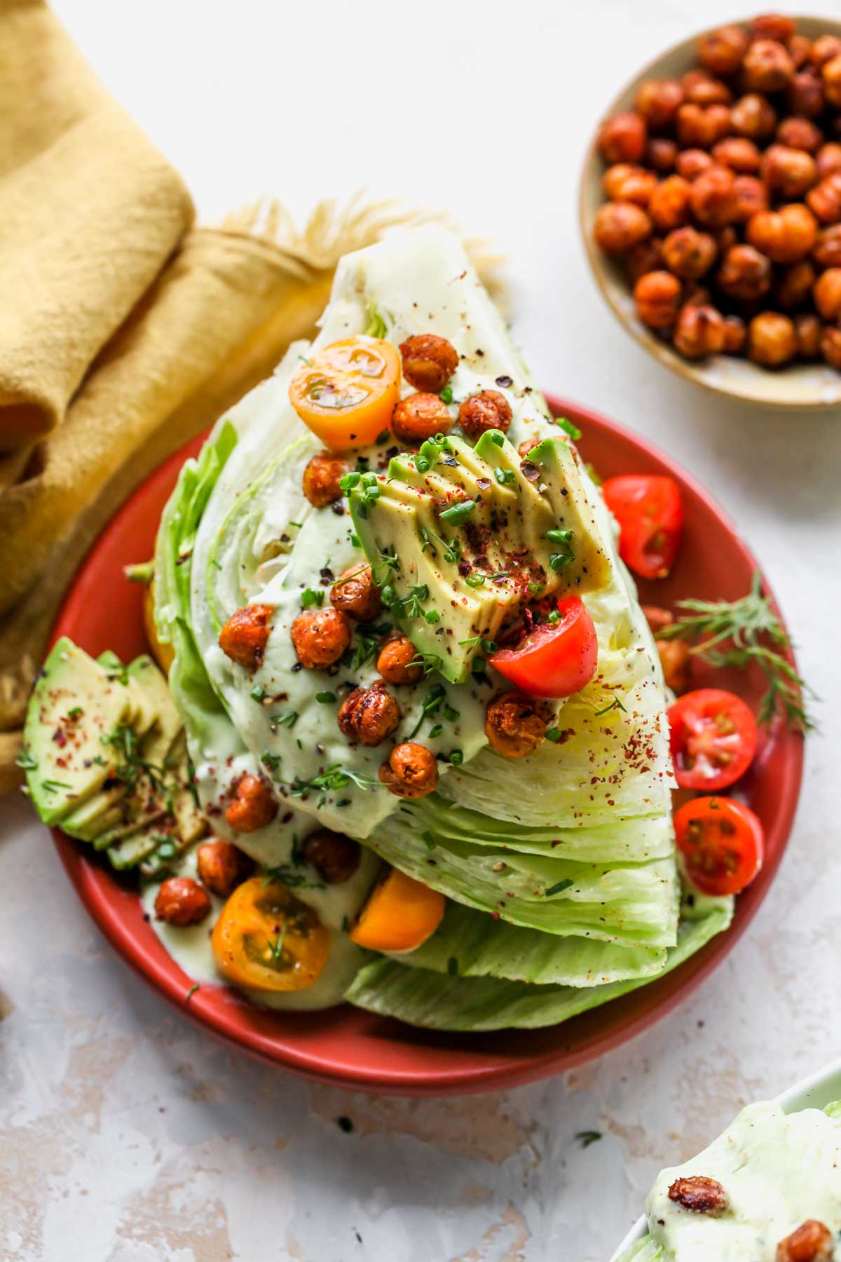 One wedge salad on an orange plate topped with avocado slices and chickpeas
