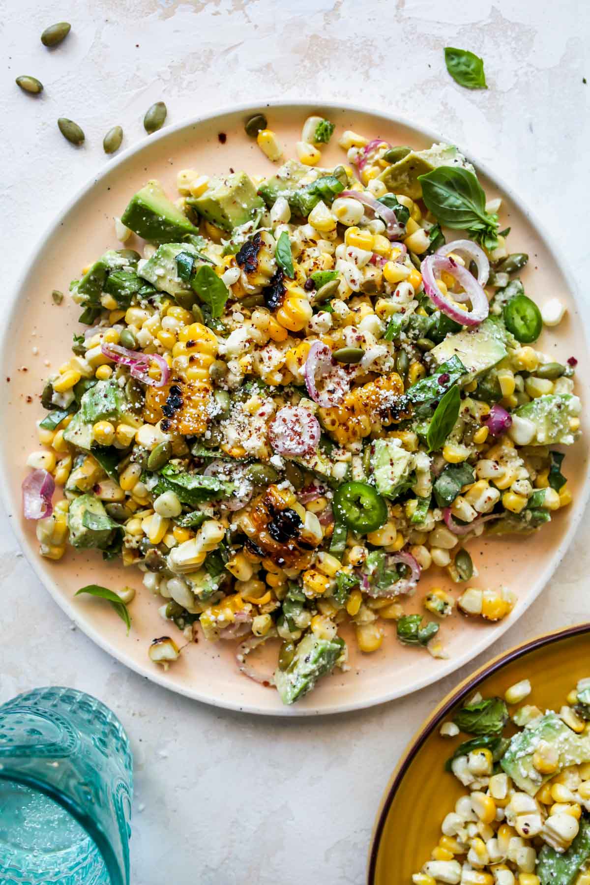 A serving platter filled with corn and avocado salad and topped with fresh herbs
