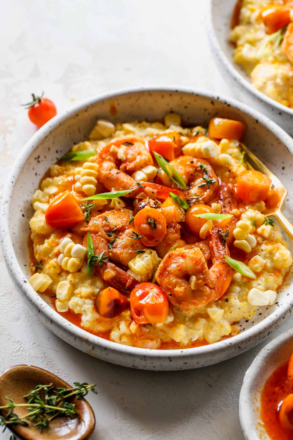 Shrimp and grits being assembled in a white serving bowl