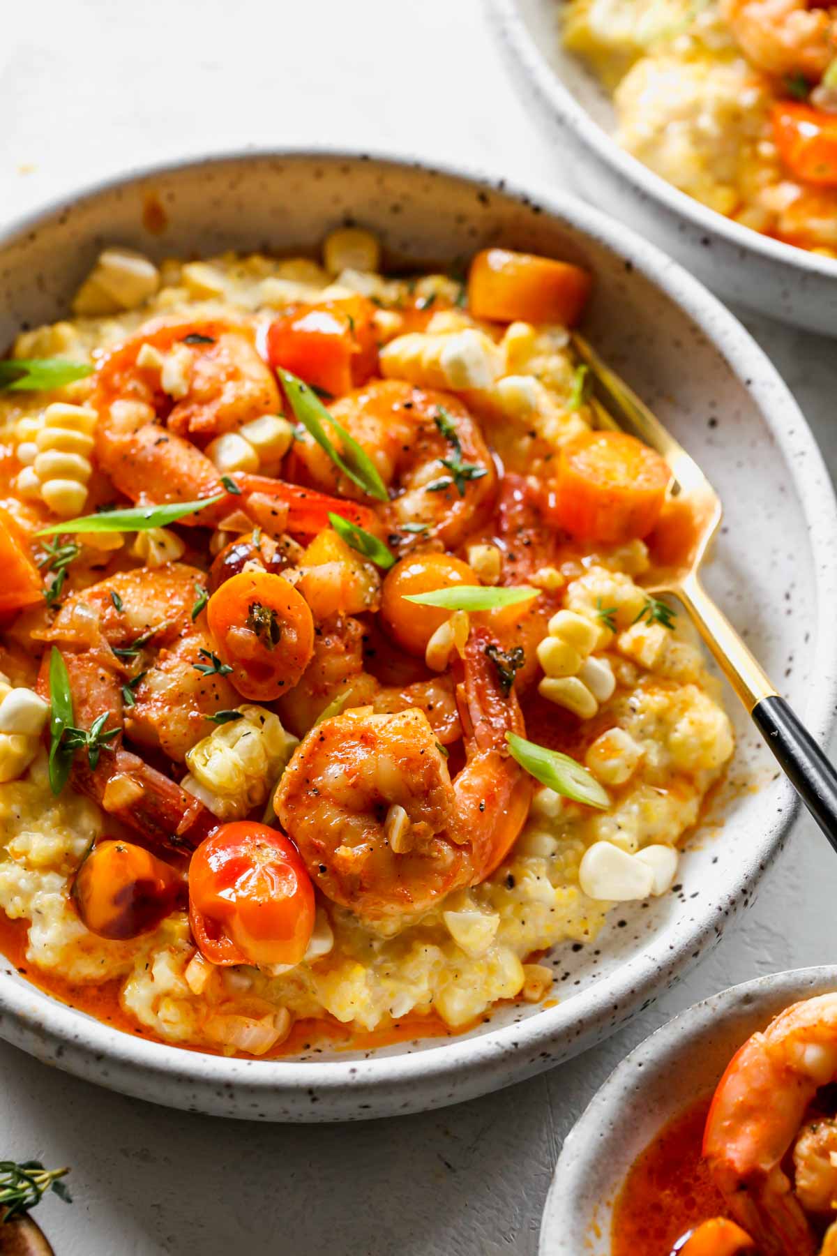 A fork taking a bite out of a bowl of cajun shrimp and grits
