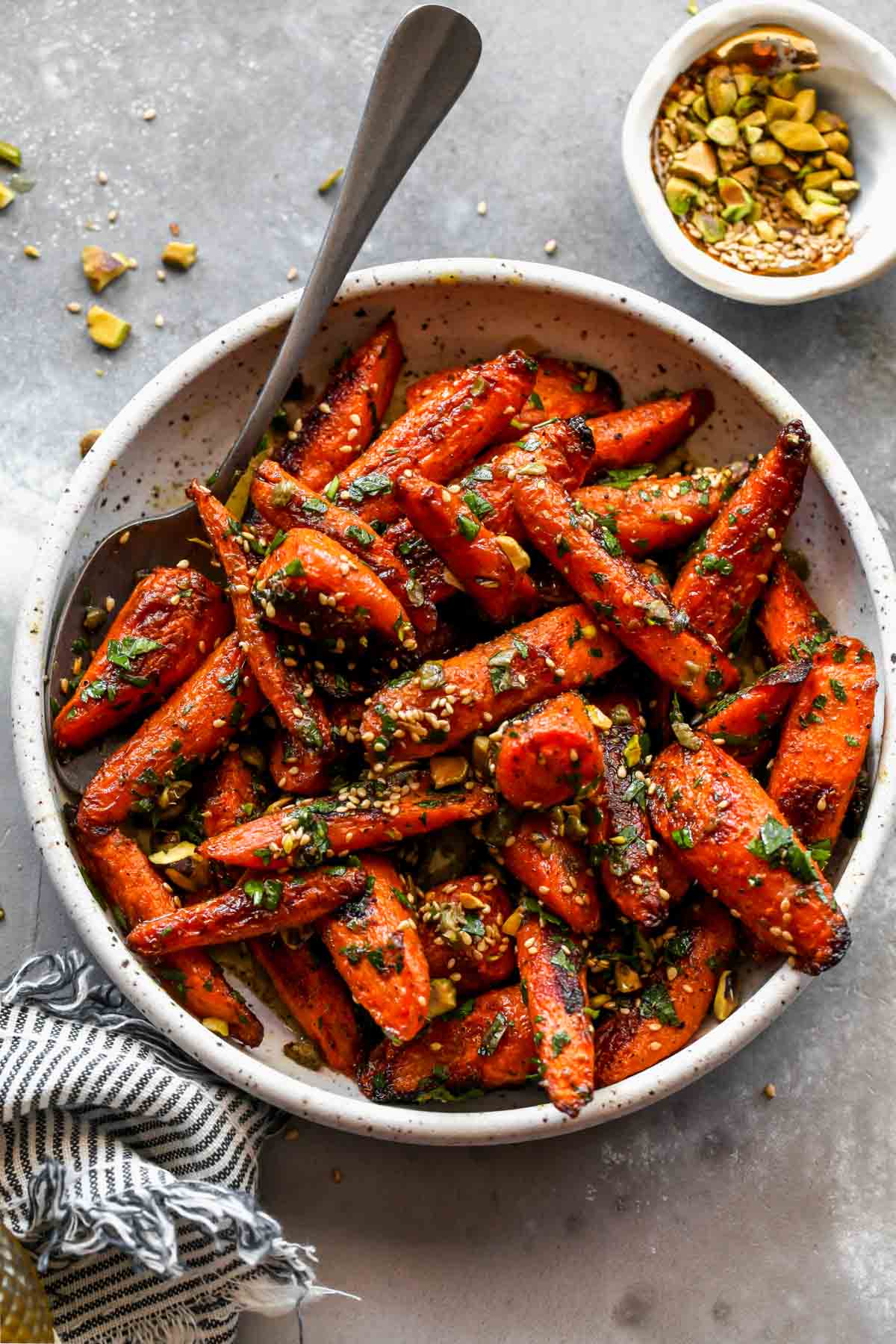 Roasted carrots in a white bowl topped with parsley, sesame seeds, and pistachios.