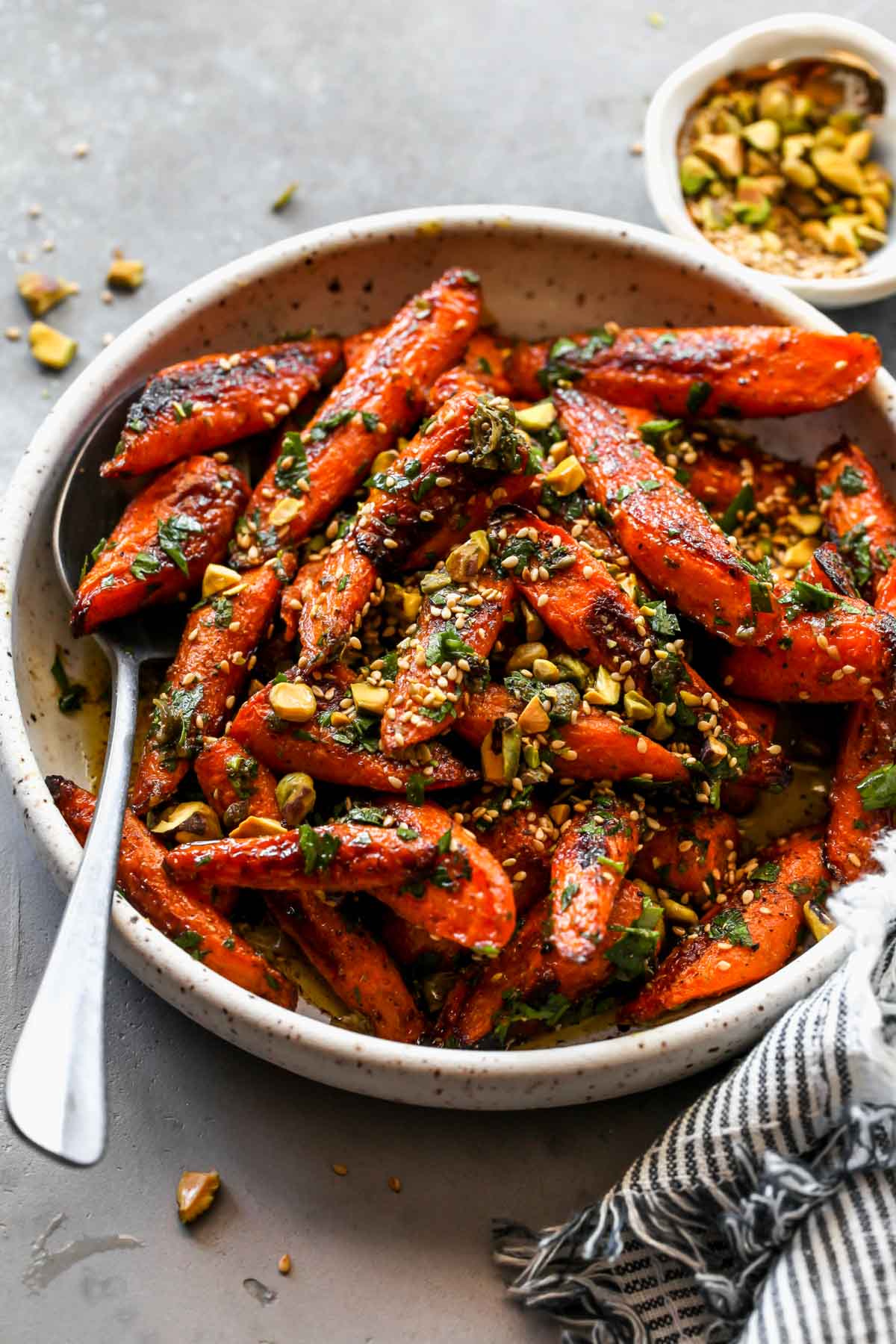Spice roasted carrots topped with nuts and seeds in a white bowl.