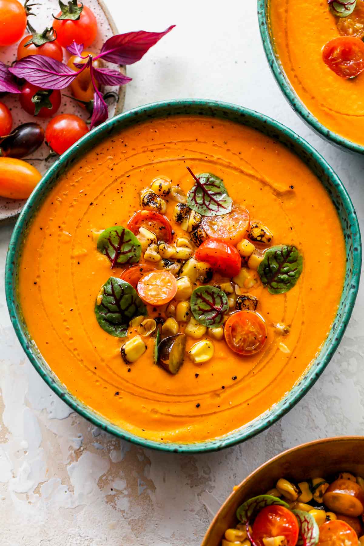 A bowl of creamy tomato soup in a blue bowl topped with corn salsa and basil
