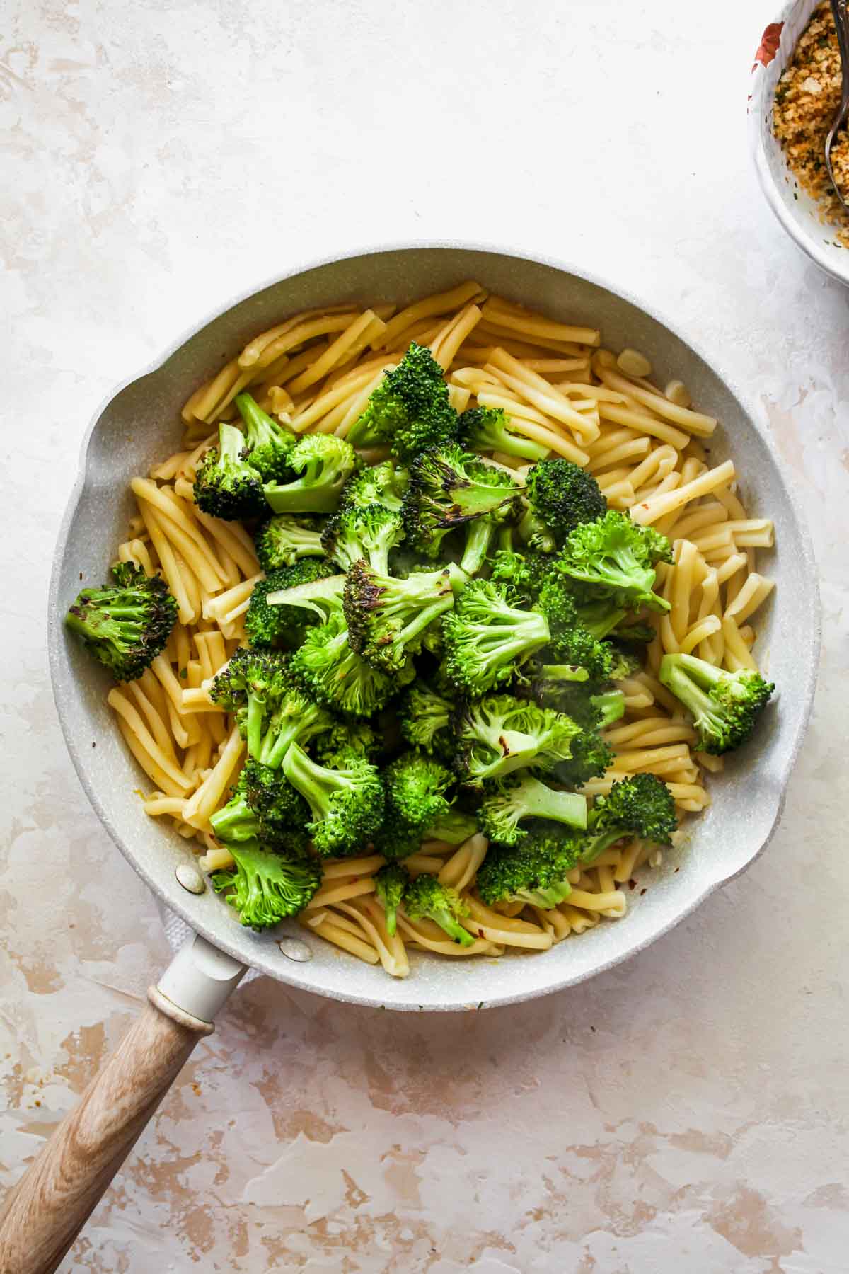Broccoli florets being added to a skillet of pasta