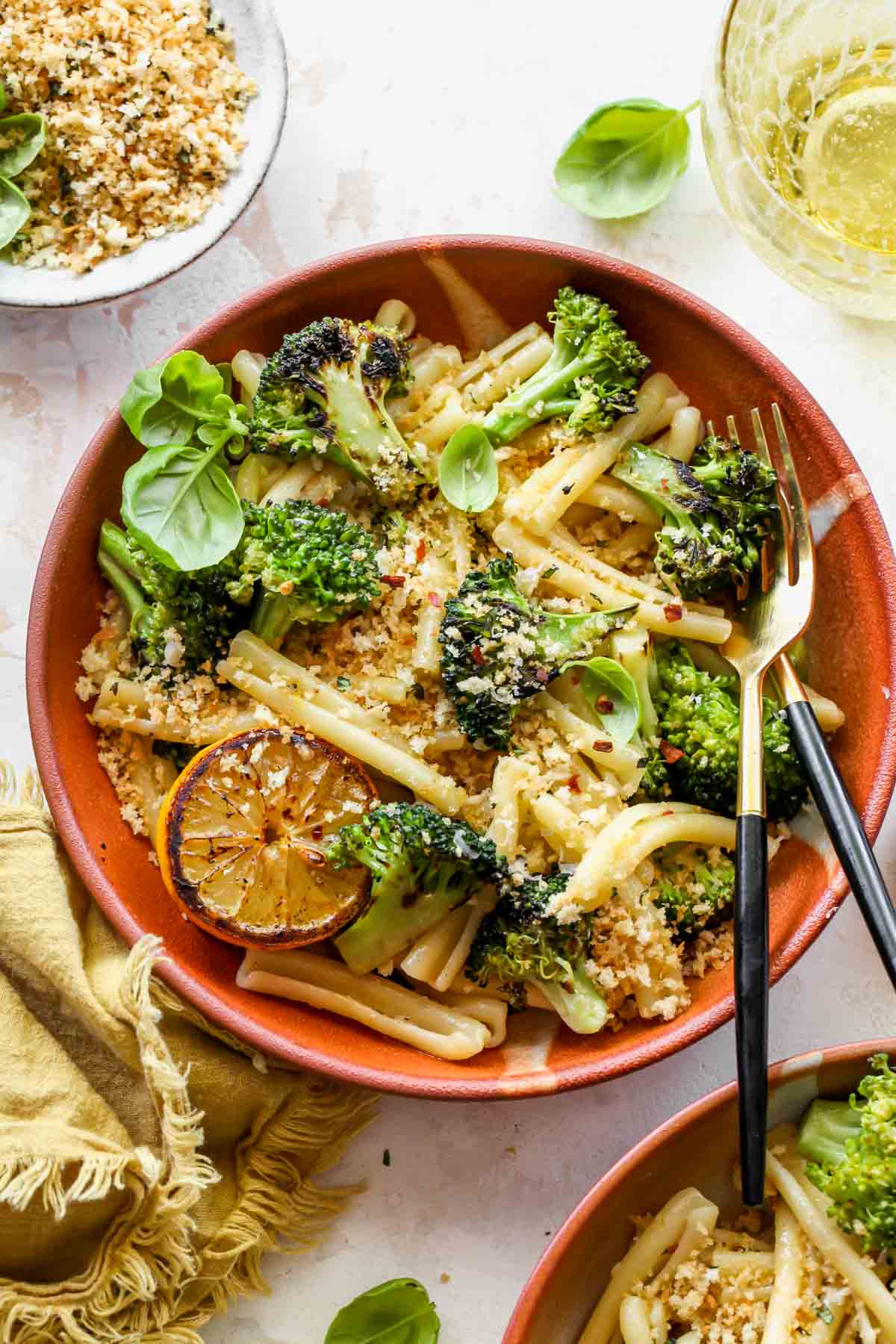 Broccoli pasta in an orange bowl topped with basil breadcrumbs and lemon slice