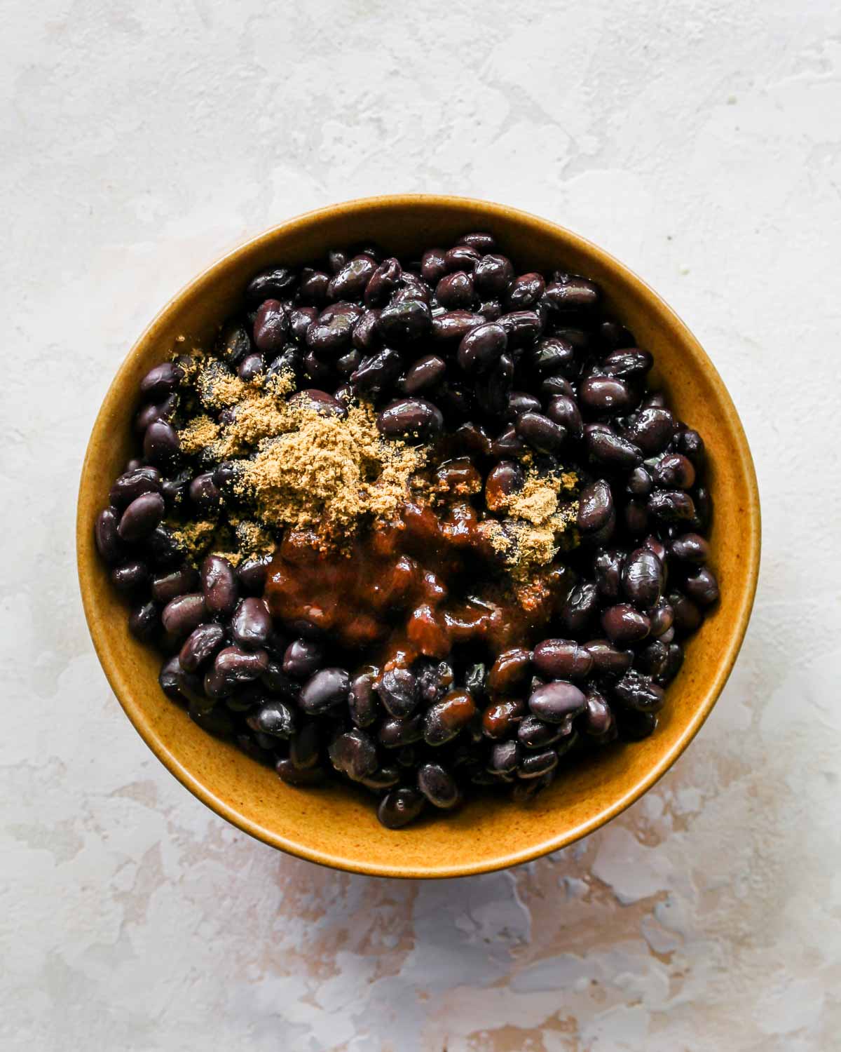 Adobo sauce being mixed into a bowl of black beans