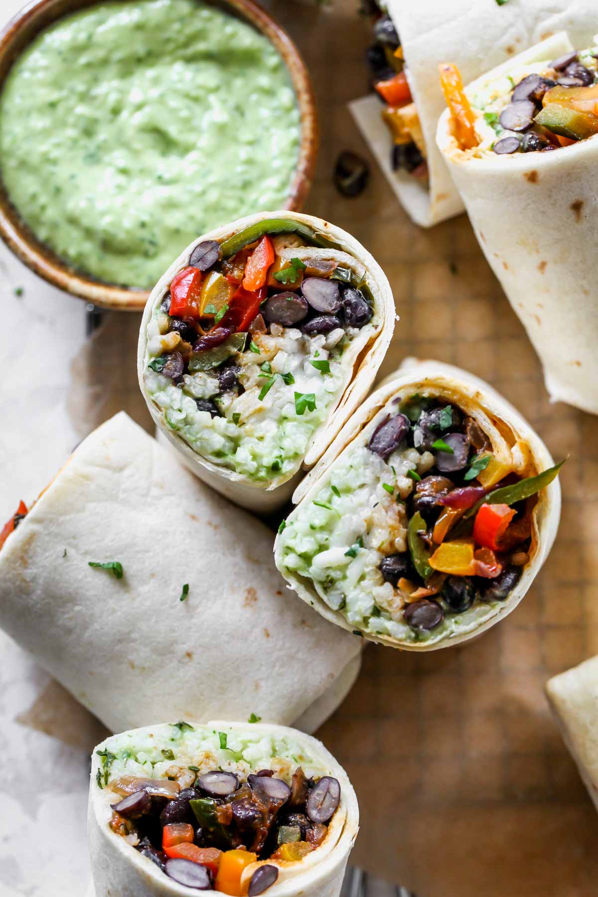 Two veggie burritos sliced in half and served on a platter with avocado sauce