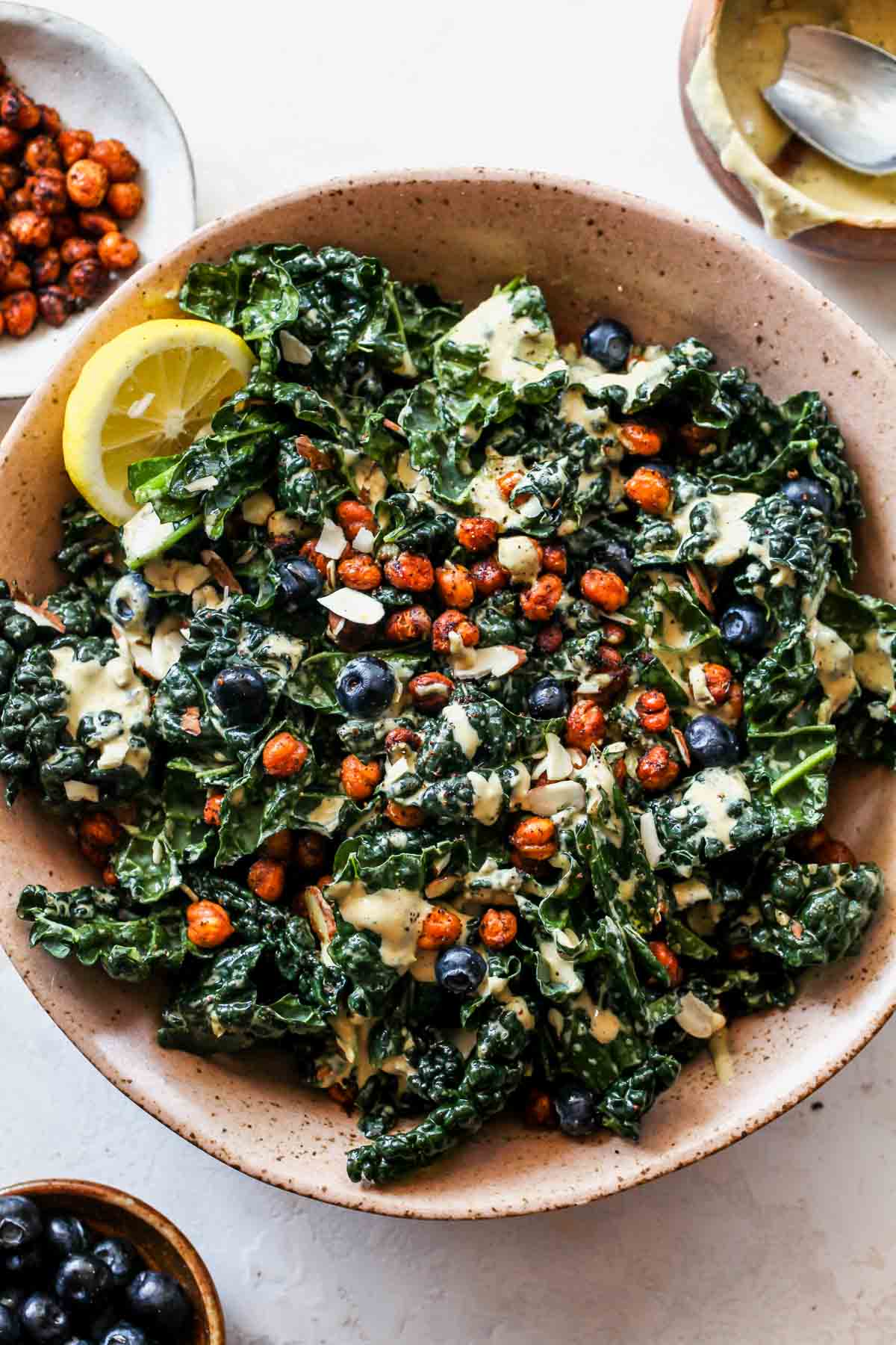 Tahini caesar salad dressing poured over salad in a large serving bowl with utensils