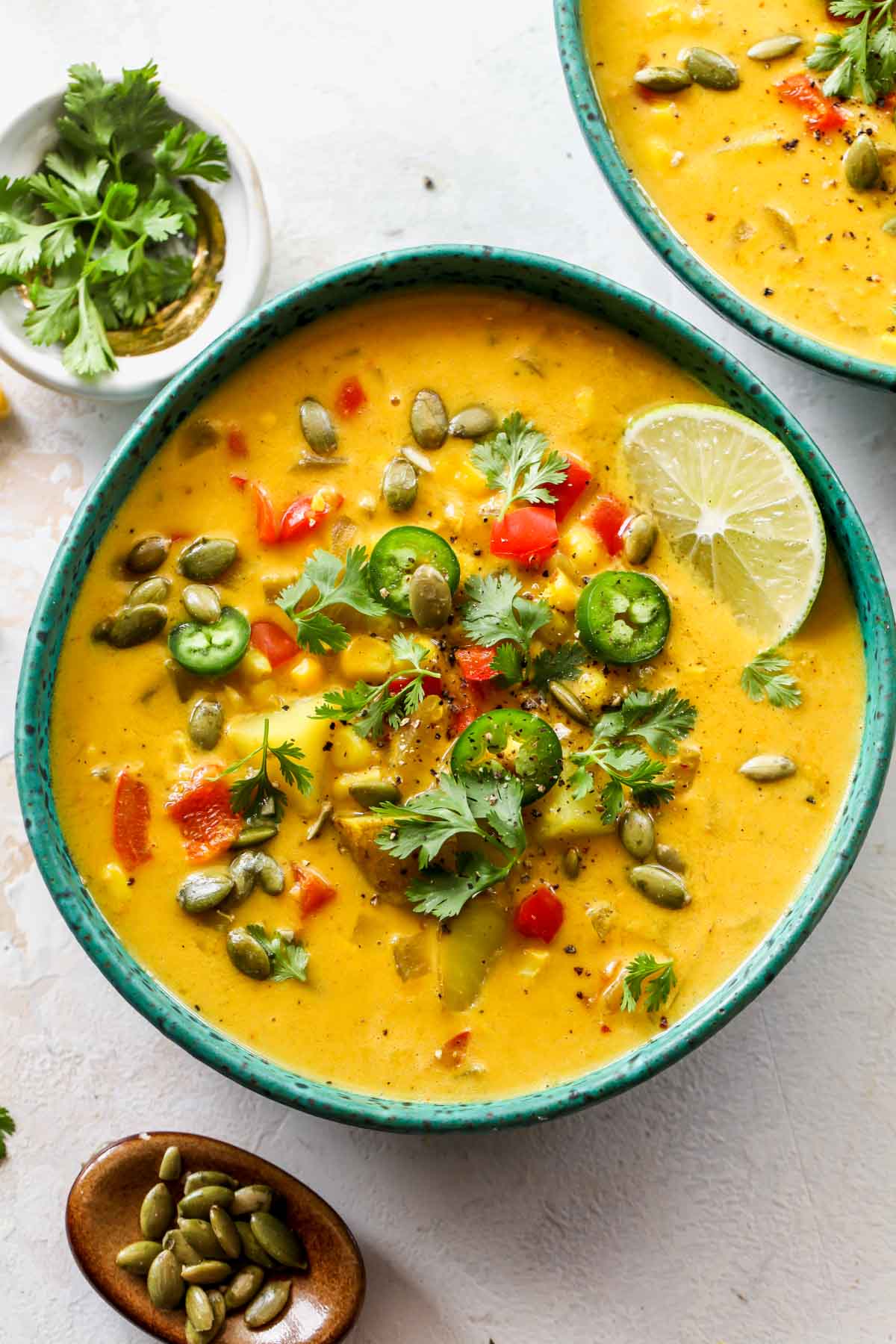 Corn chowder in a teal bowl topped with cilantro and pumpkin seeds