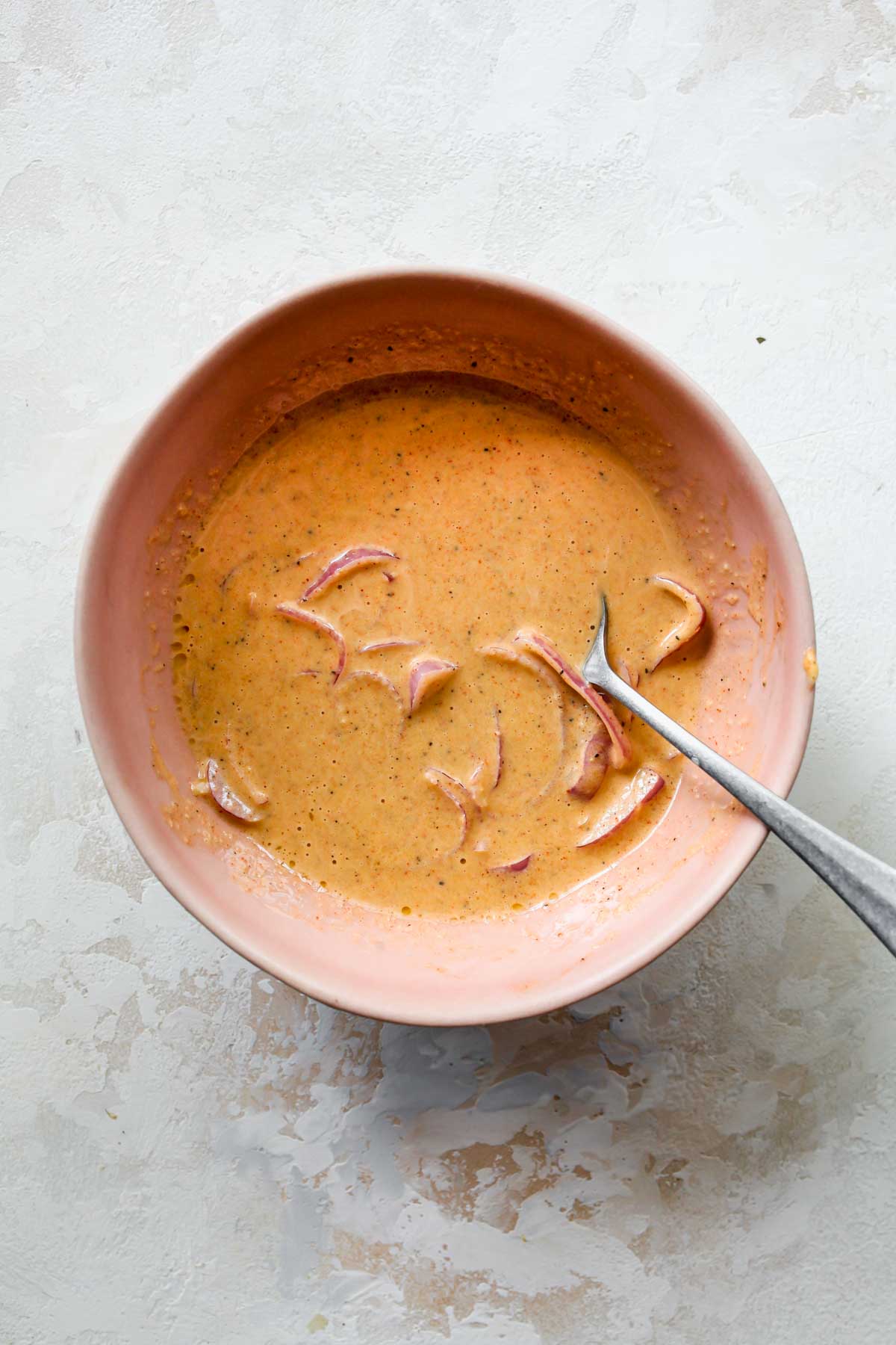 mayonnaise, olive oil, lemon juice, vinegar, garlic powder, paprika, salt, and pepper being whisked in a bowl