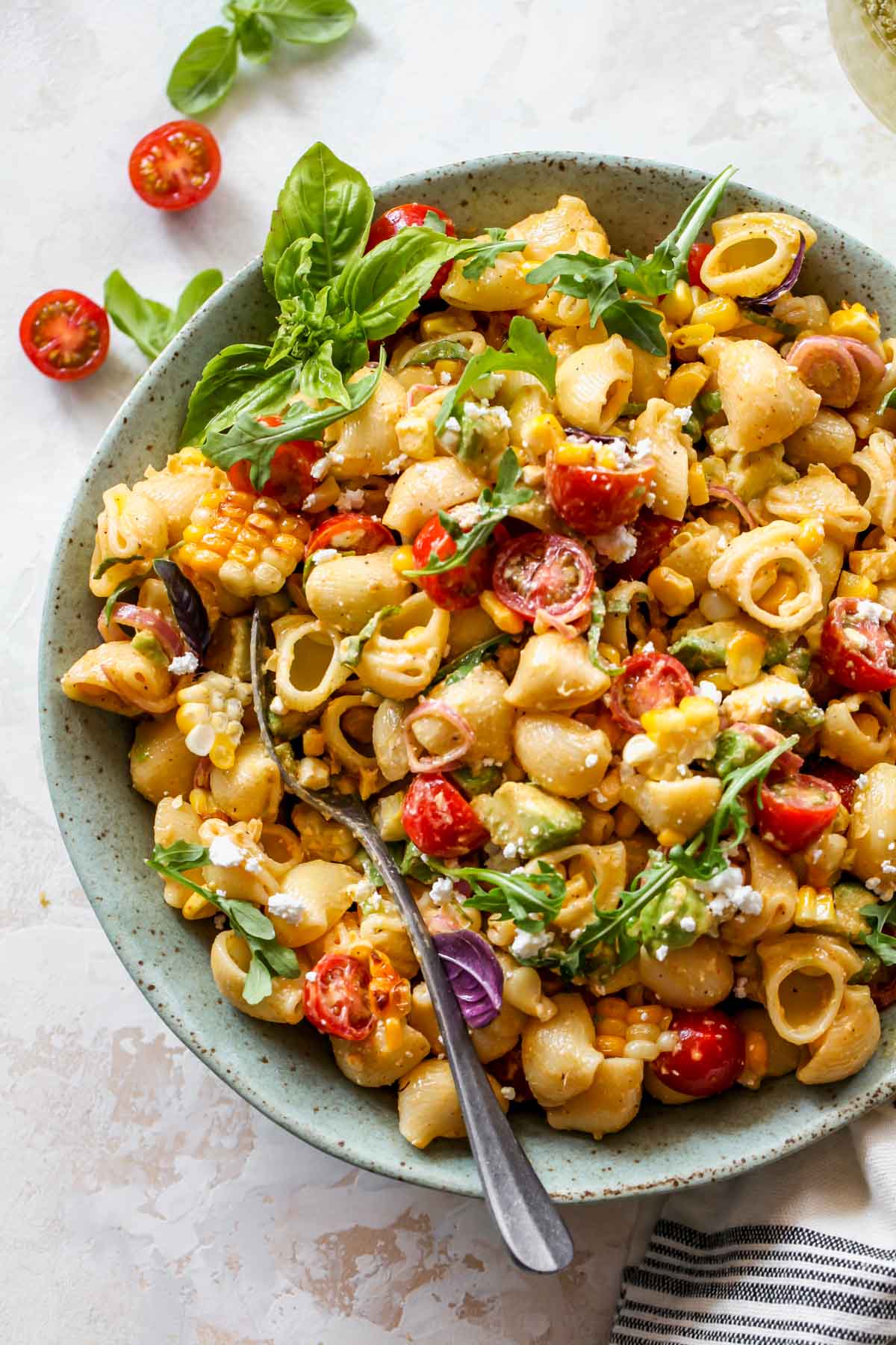 Macaroni salad in a green bowl with tomatoes, avocado, corn, and basil