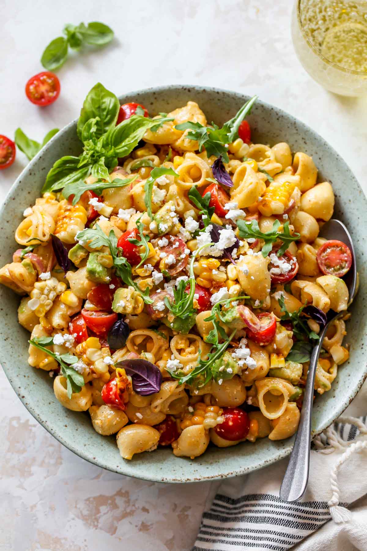 Corn and basil macaroni salad styled in a bowl topped with fresh basil and cheese.
