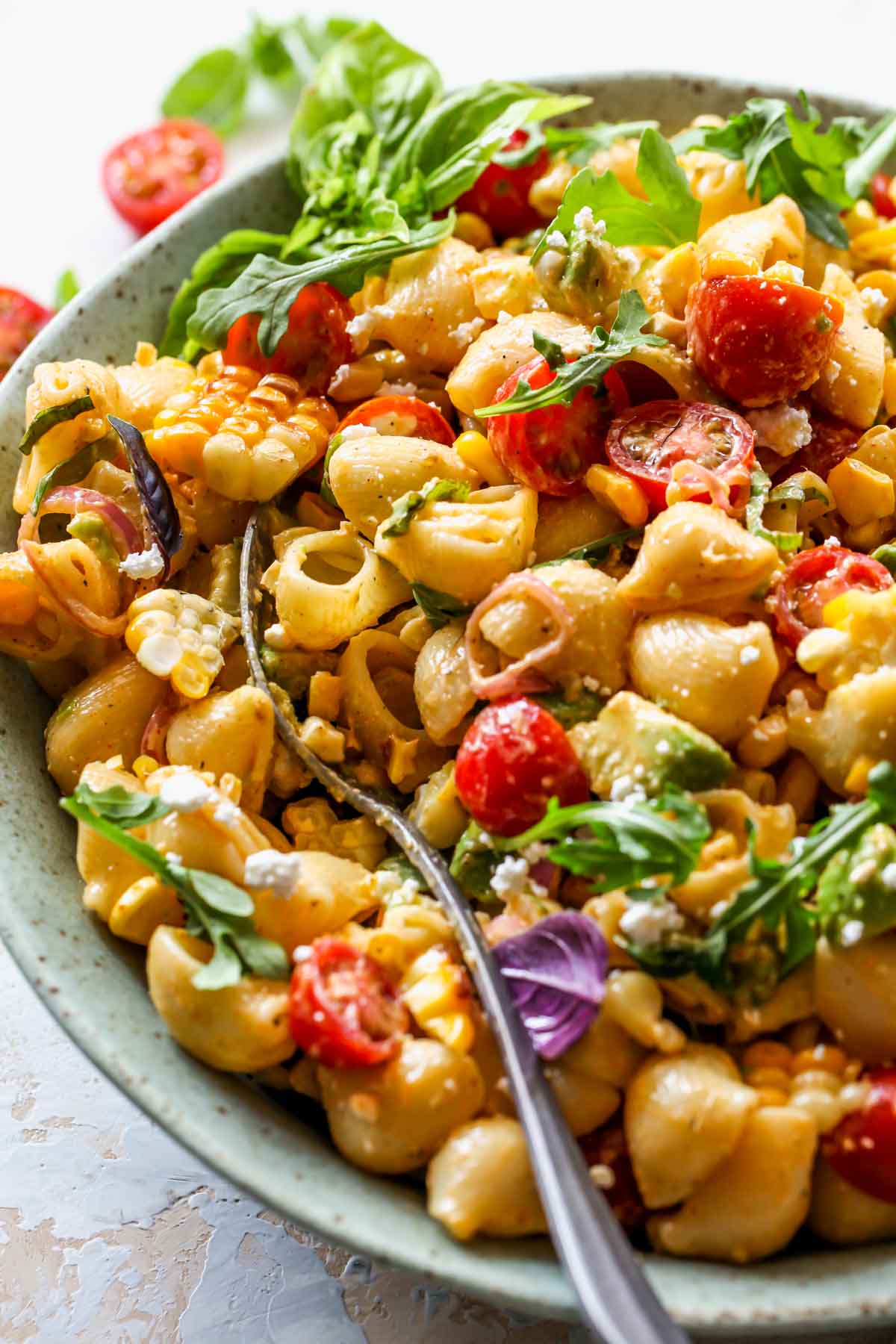 A serving spoon scooping a portion of pasta salad out of a bowl