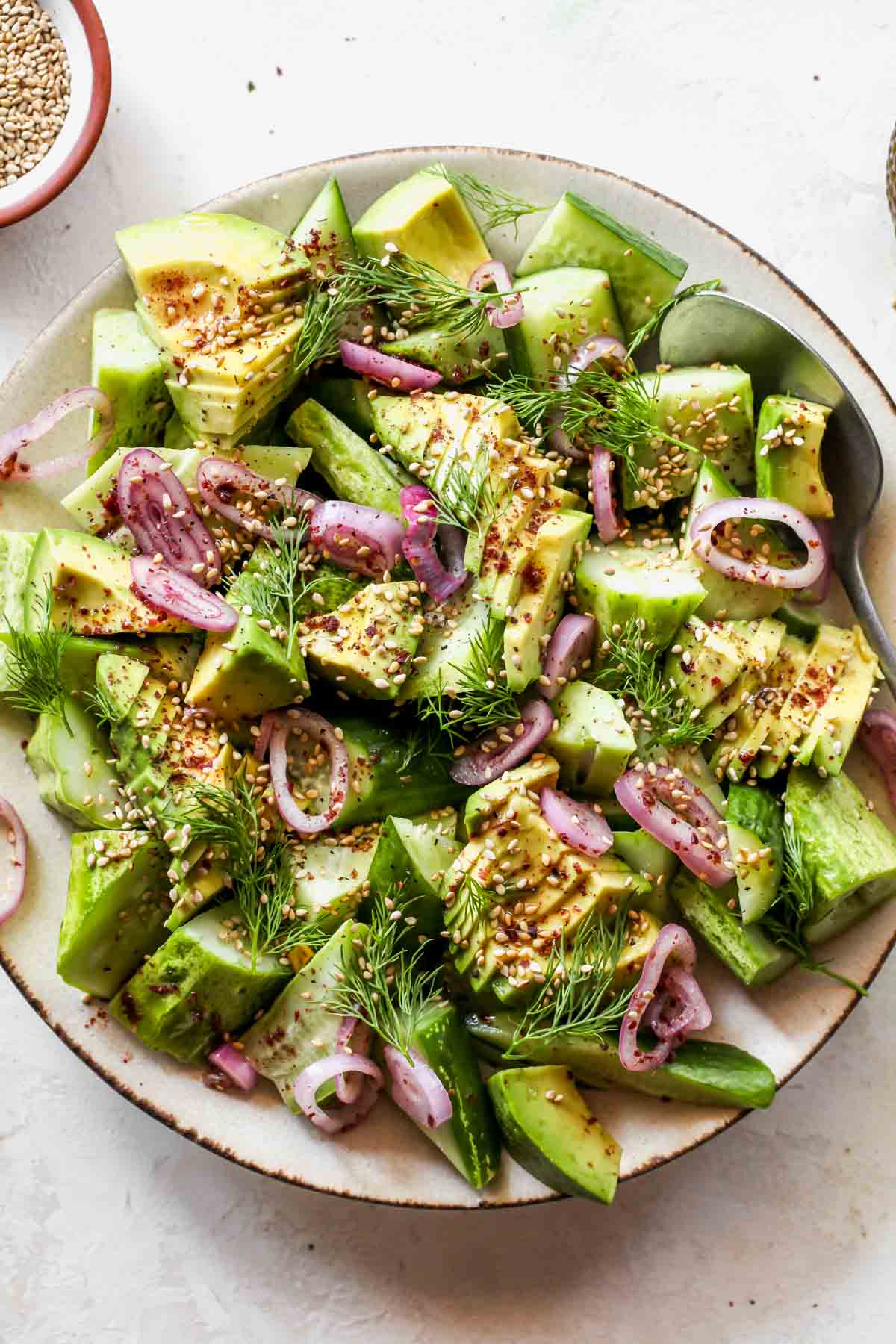 Cucumber and avocado salad topped with shallots, dill, and sesame seeds on a platter