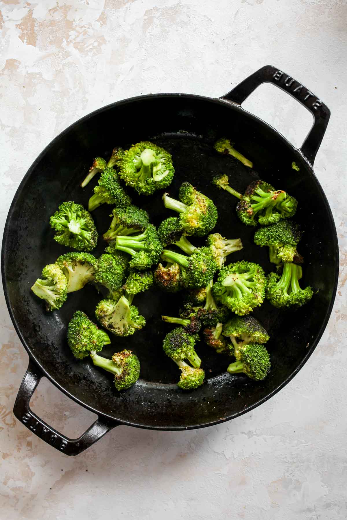 Broccoli florets being sautéed in a black pan.