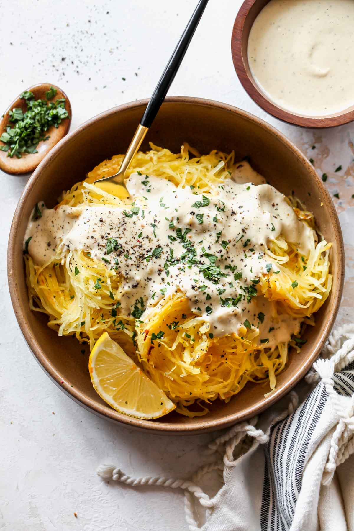 Spaghetti squash in a tan bowl topped with vegan alfredo sauce and parsley