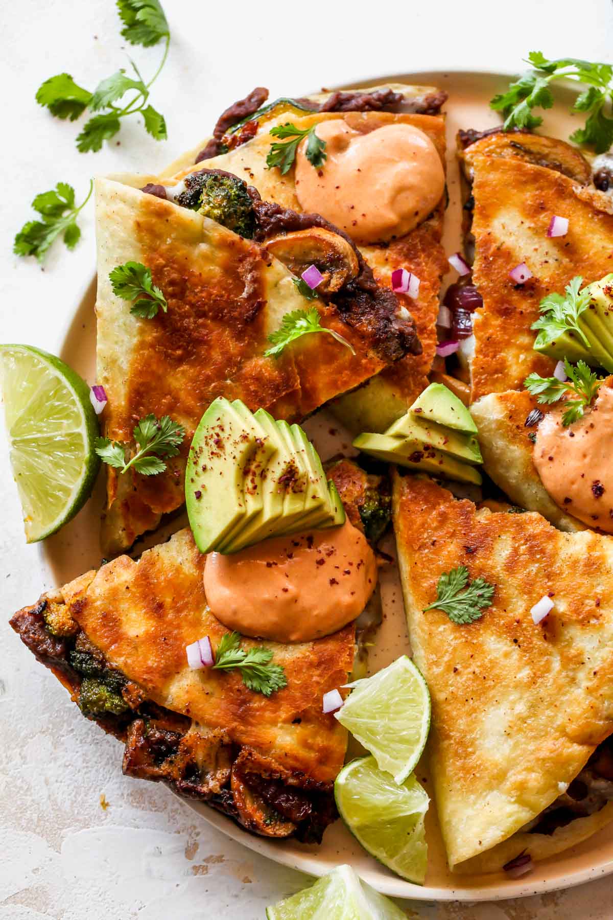 A plate of sliced quesadillas topped with yogurt sauce and avocado slices