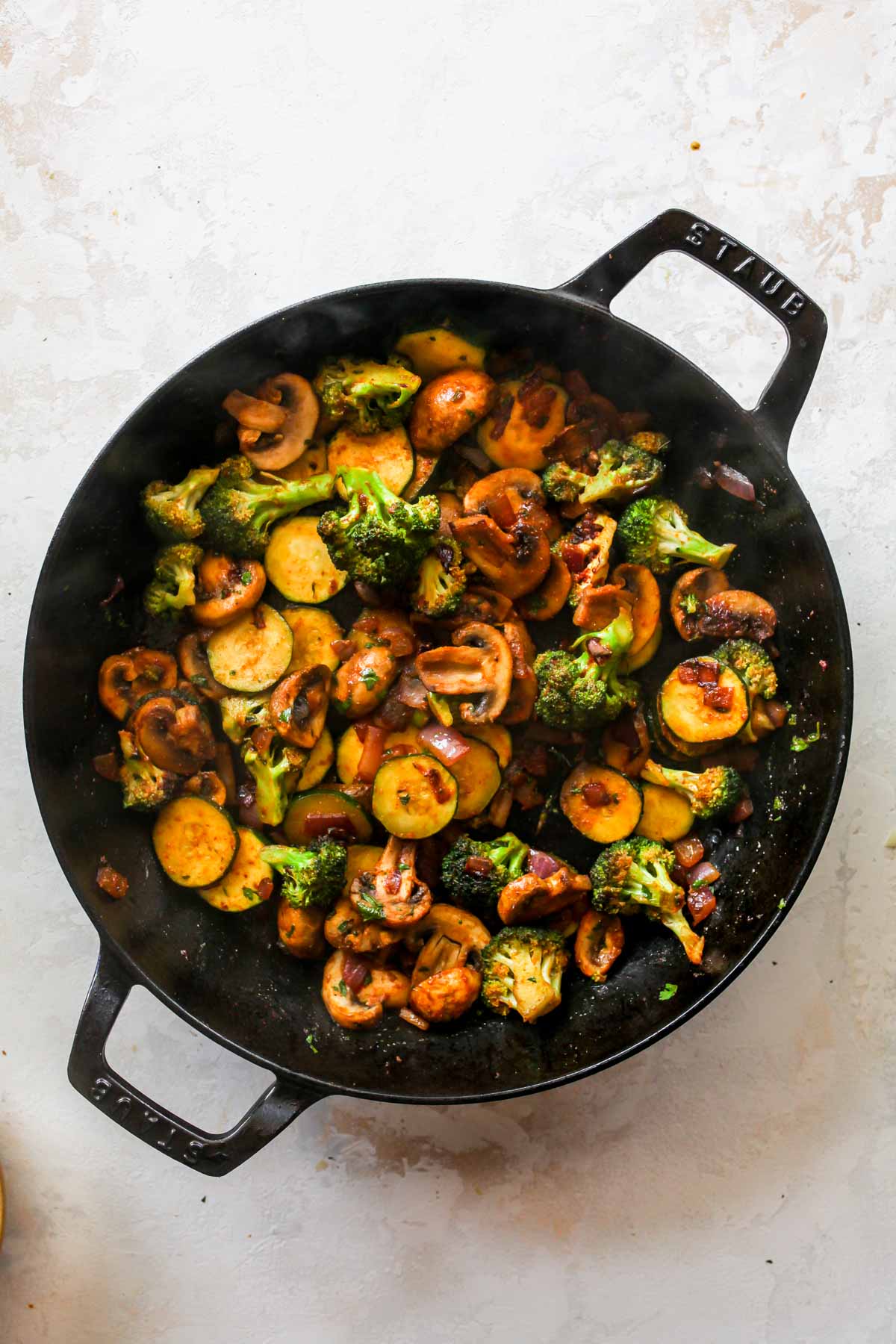 Mushrooms, broccoli, zucchini, and red onion sautéing in a skillet
