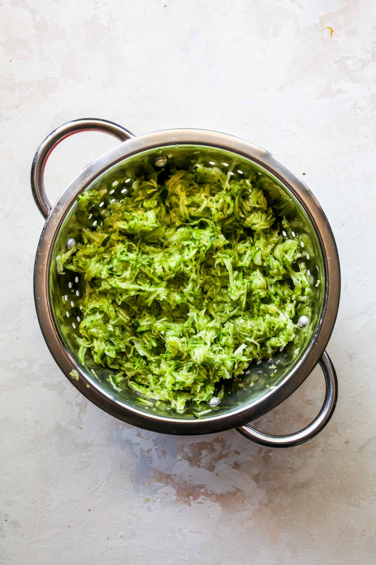 Shredded zucchini being strained in a colander