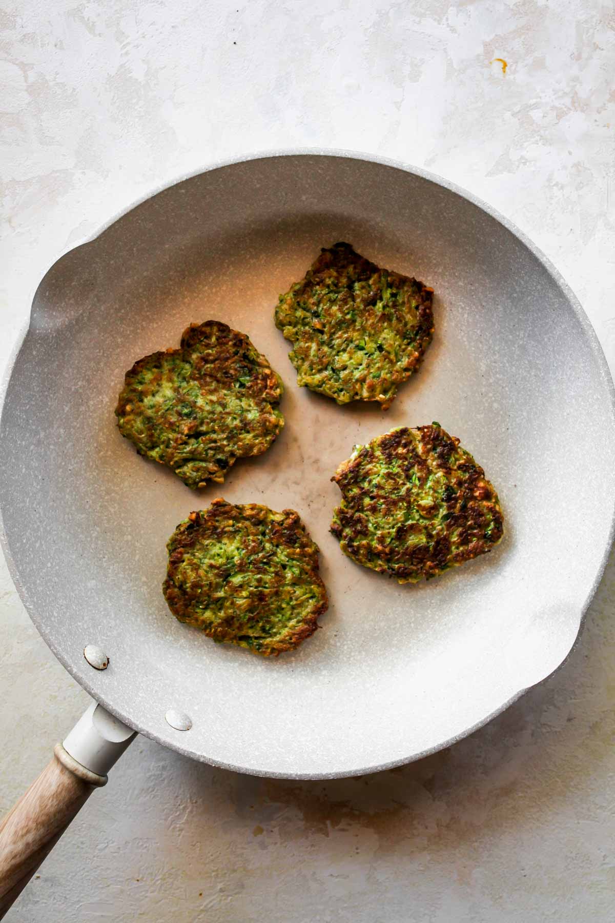 Zucchini fritters being sautéed in a white skillet