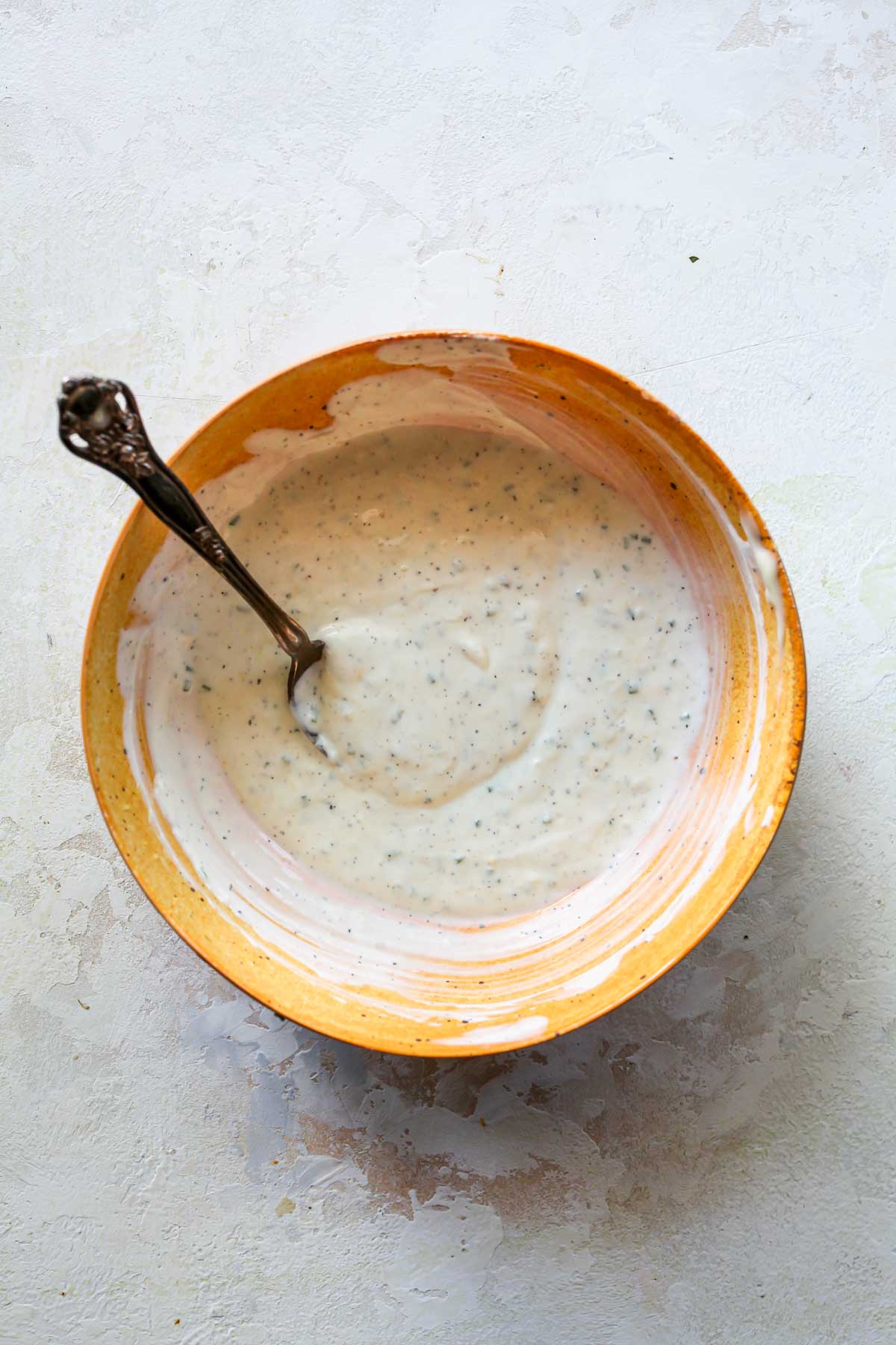 Creamy garlic-herb sauce being mixed in an orange bowl