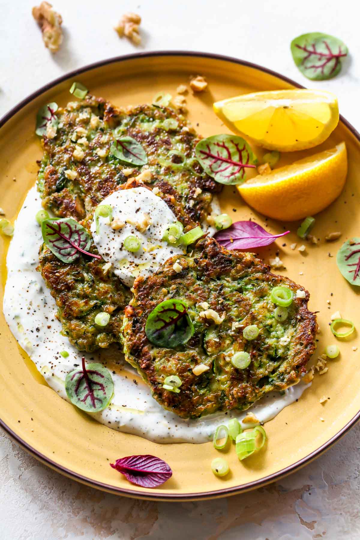 Zucchini fritters arranged on a plate with garlic sauce and lemons