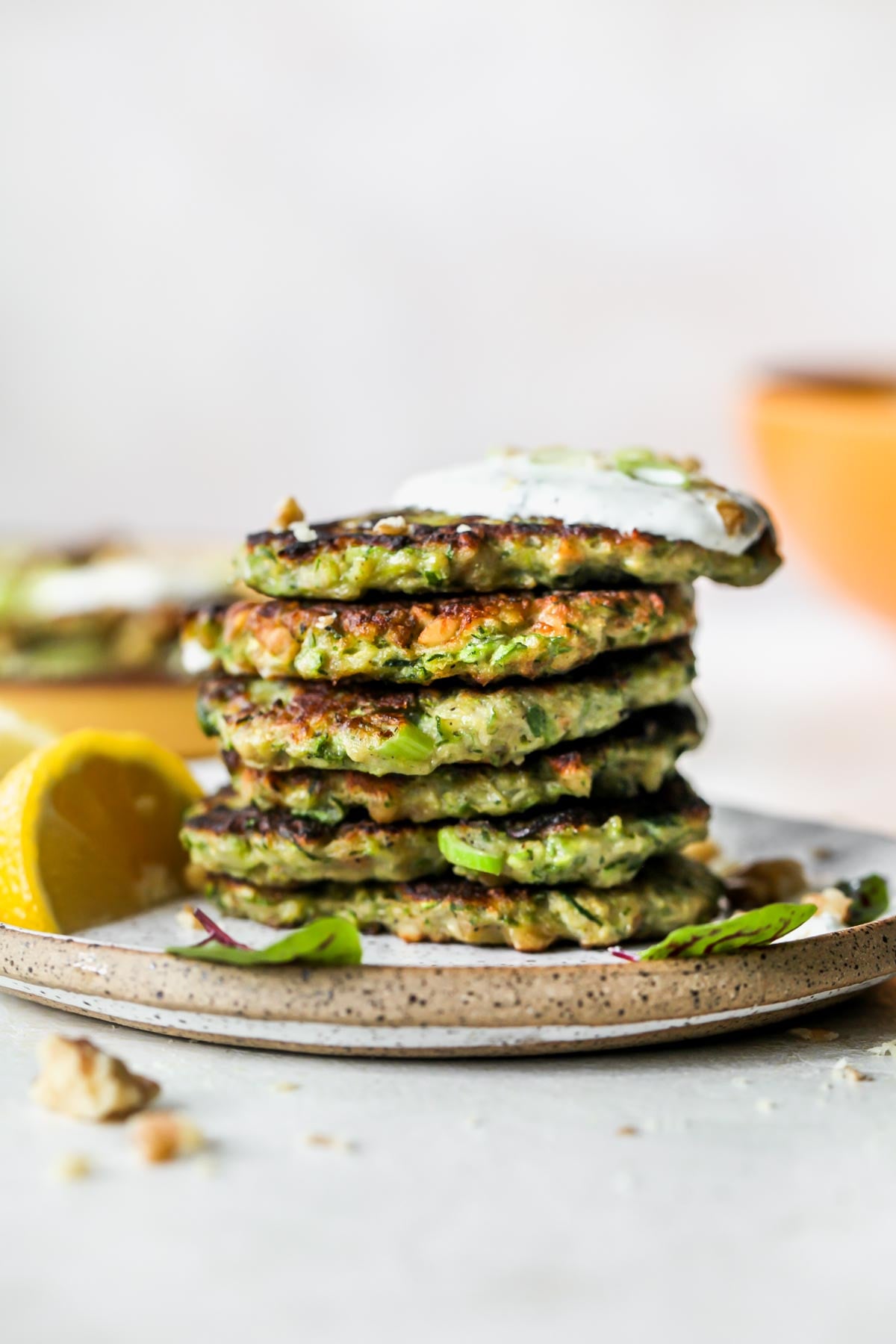 A stack of zucchini fritters on a plate topped with garlic sauce