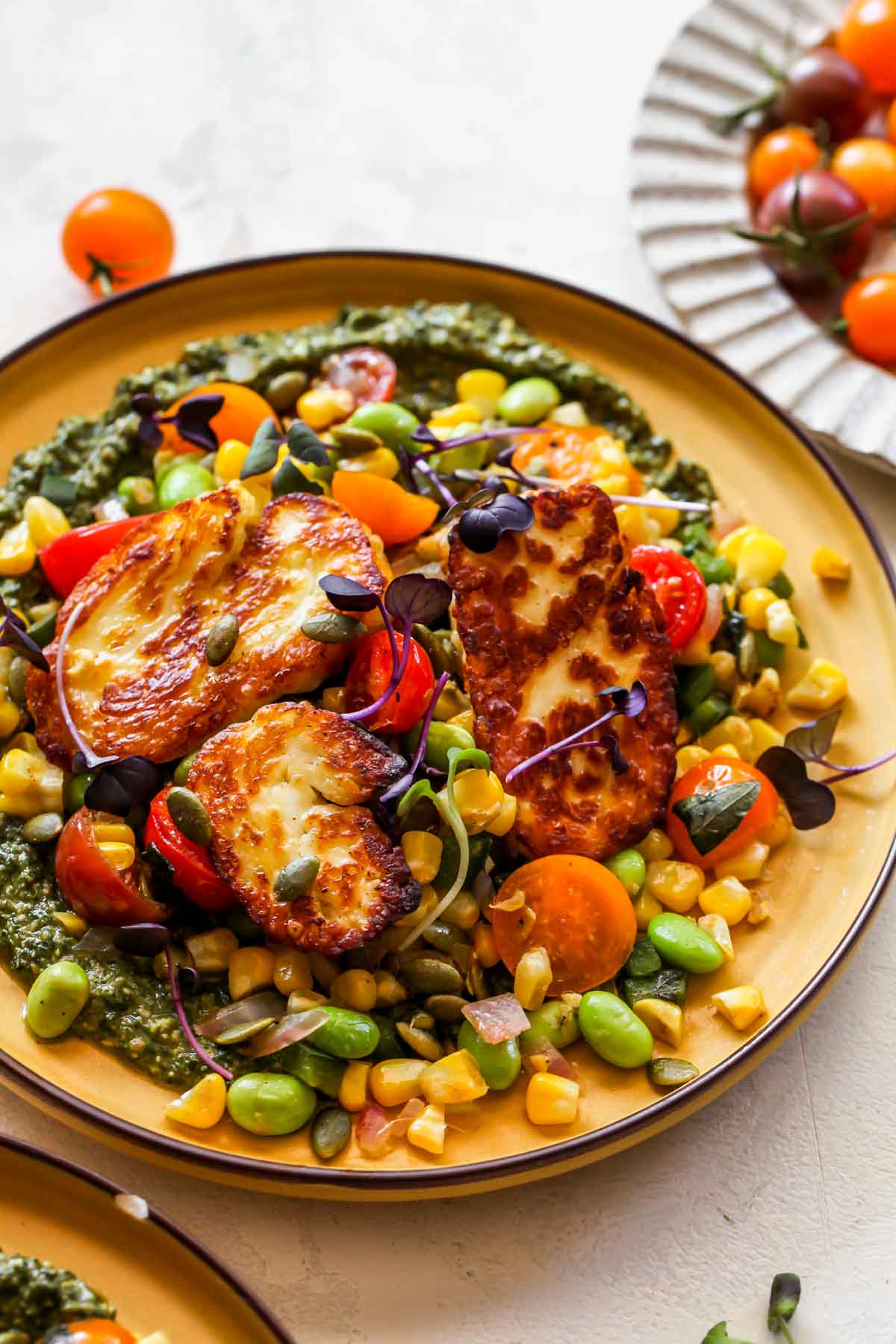Succotash and halloumi styled on a yellow plate with pesto