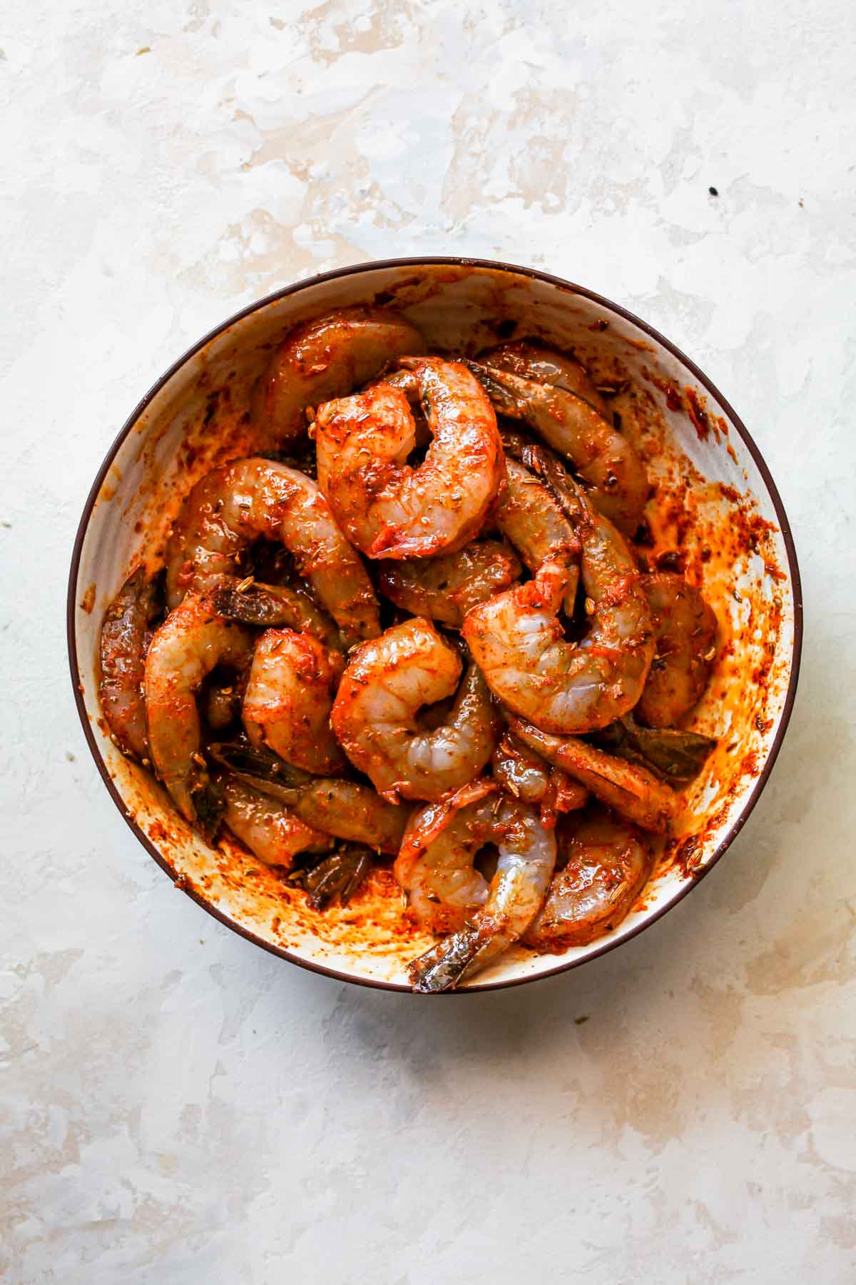 Raw shrimp in a white bowl tossed in Greek marinade