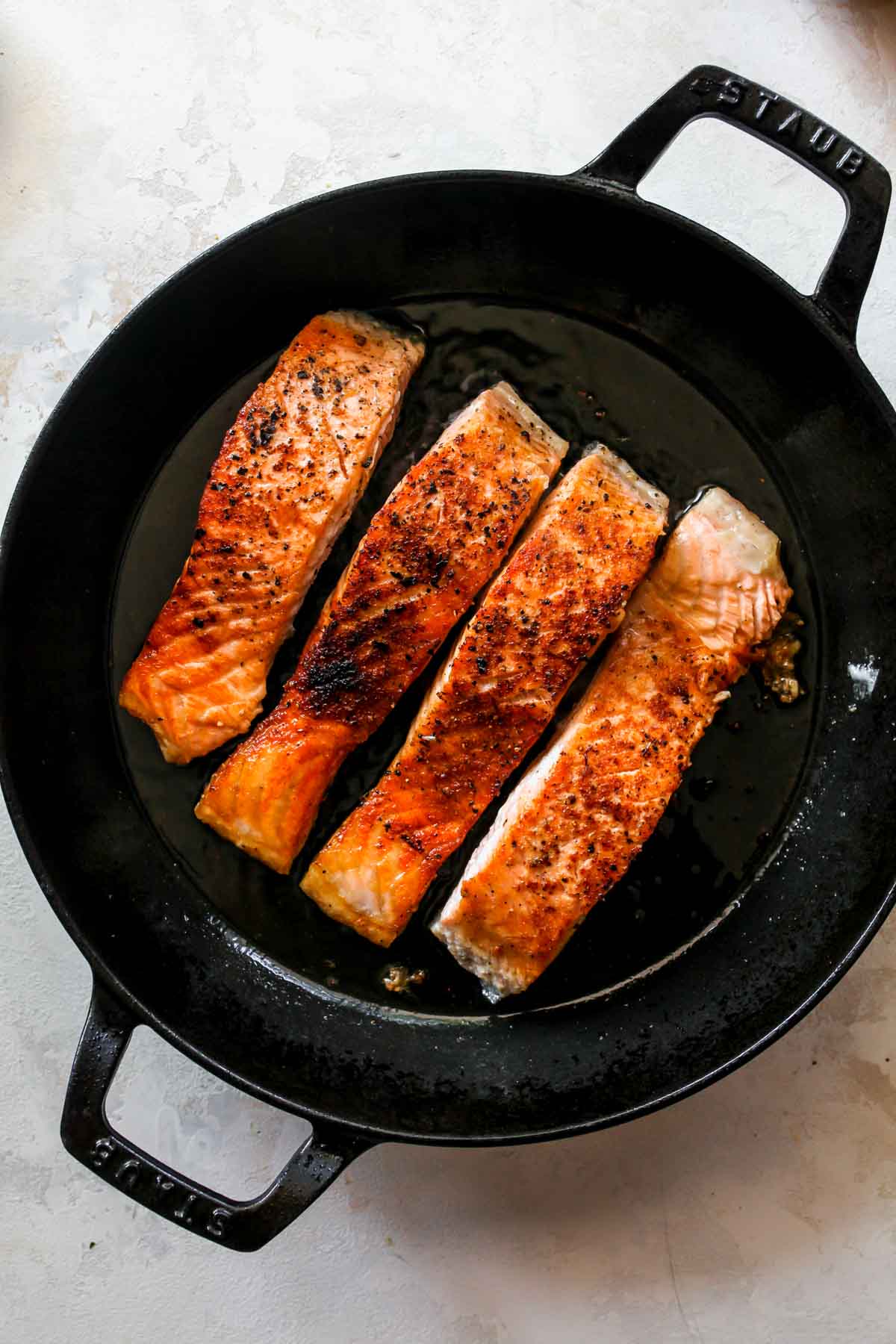 Four salmon fillets being seared in a cast iron skillet