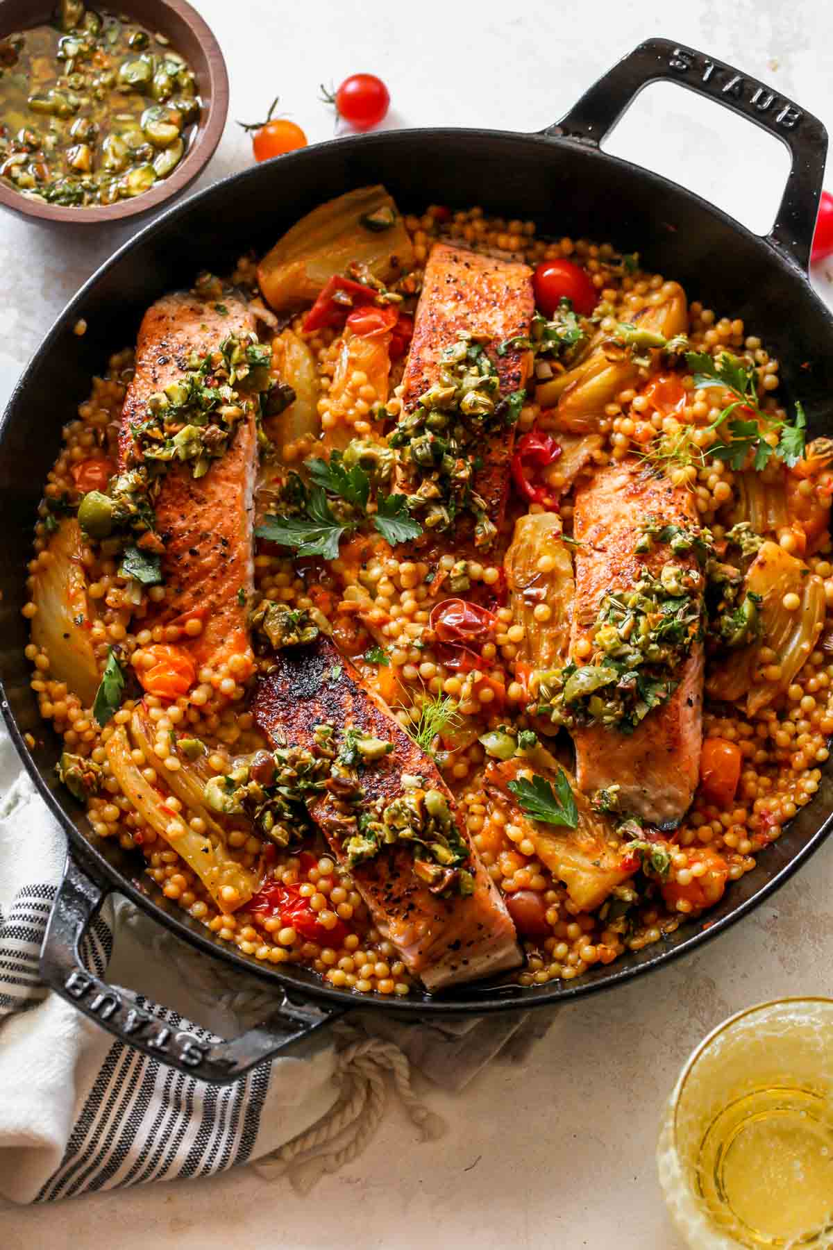 Salmon being added to a skillet of couscous, tomatoes, and fennel