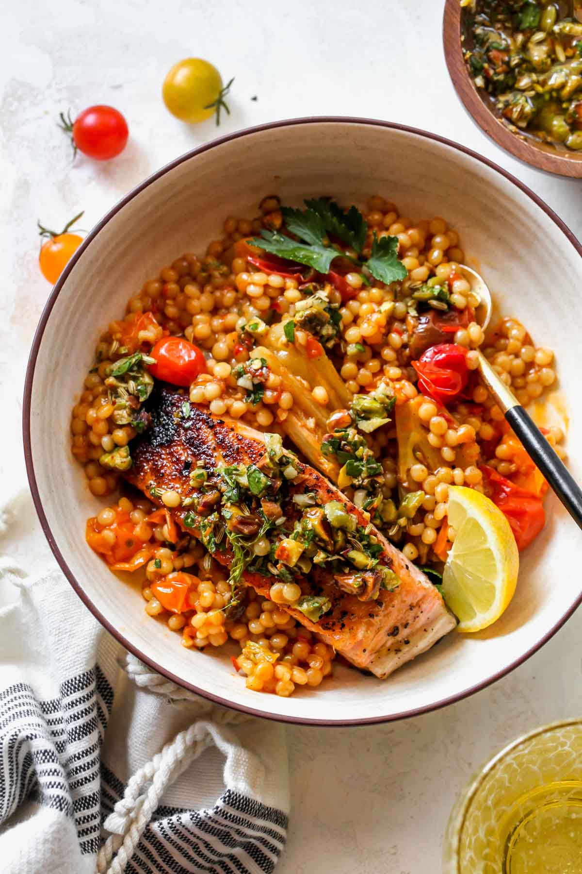 A tan bowl filled with couscous, salmon, olive salsa, and lemon