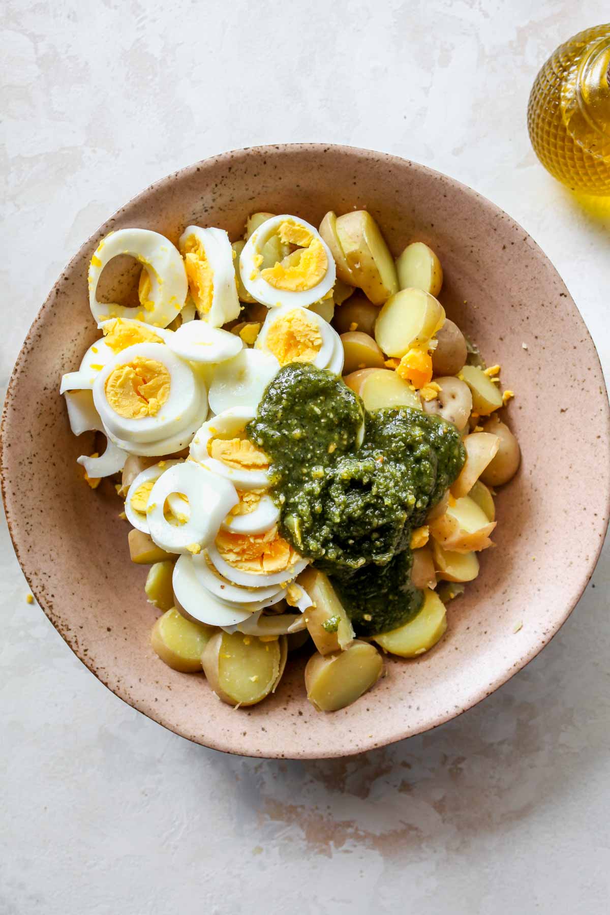 Pesto being added to a bowl of potatoes and boiled eggs