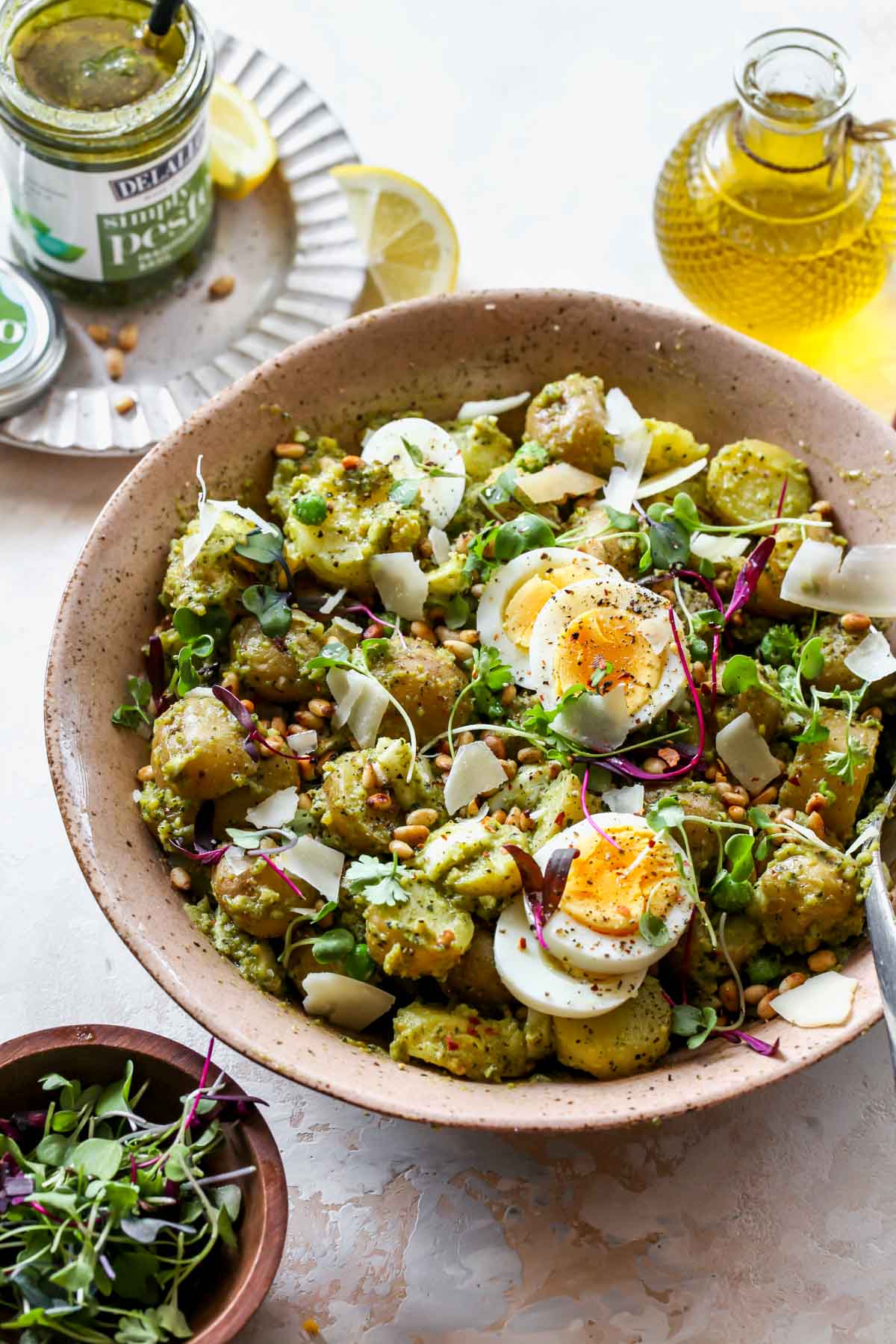 Potato salad styled in a serving bowl with jar of pesto beside it