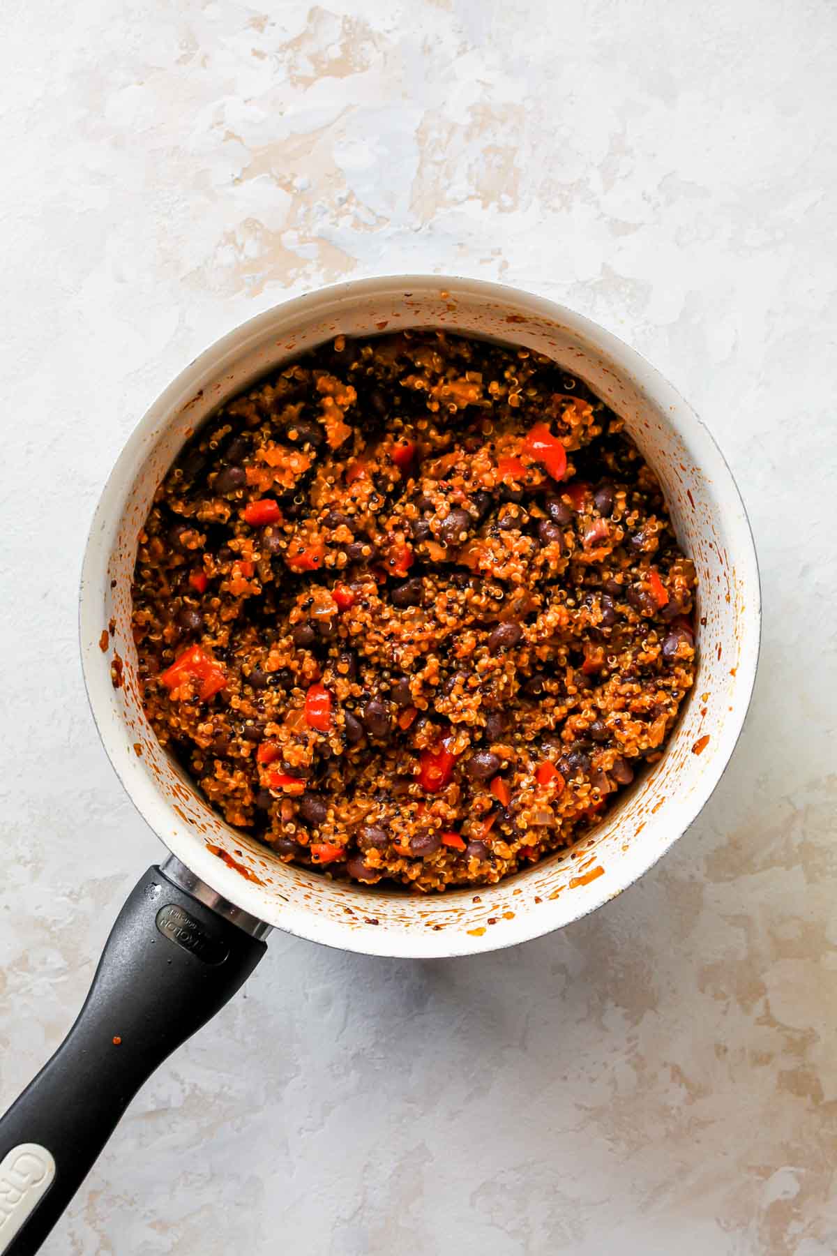 Black beans being stirred into a saucepan filled with quinoa
