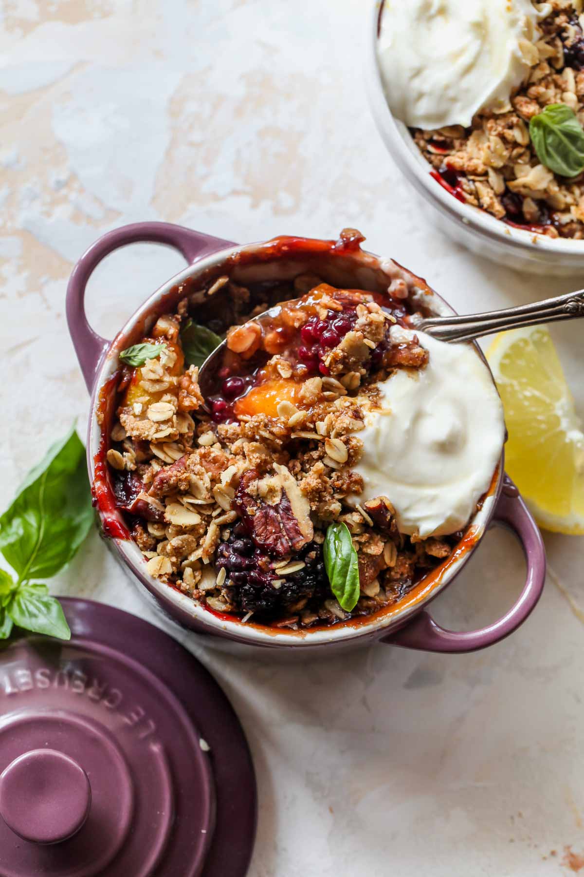 A spoon digging into a purple ramekin filled with fruit crisp