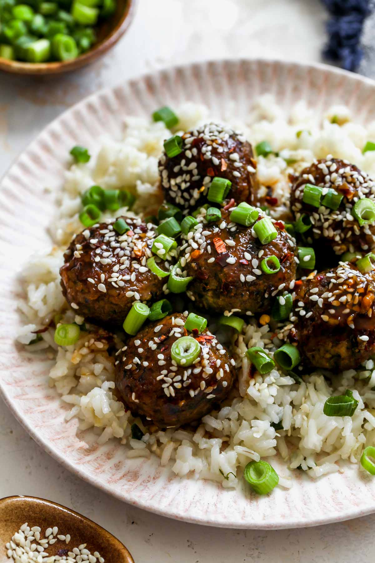 Mushroom meatballs over ginger-scallion rice on a white plate topped with sesame and scallions