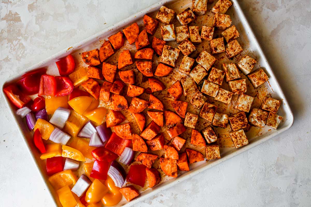 Tofu, sweet potatoes, peppers, and onions arranged on a sheet pan