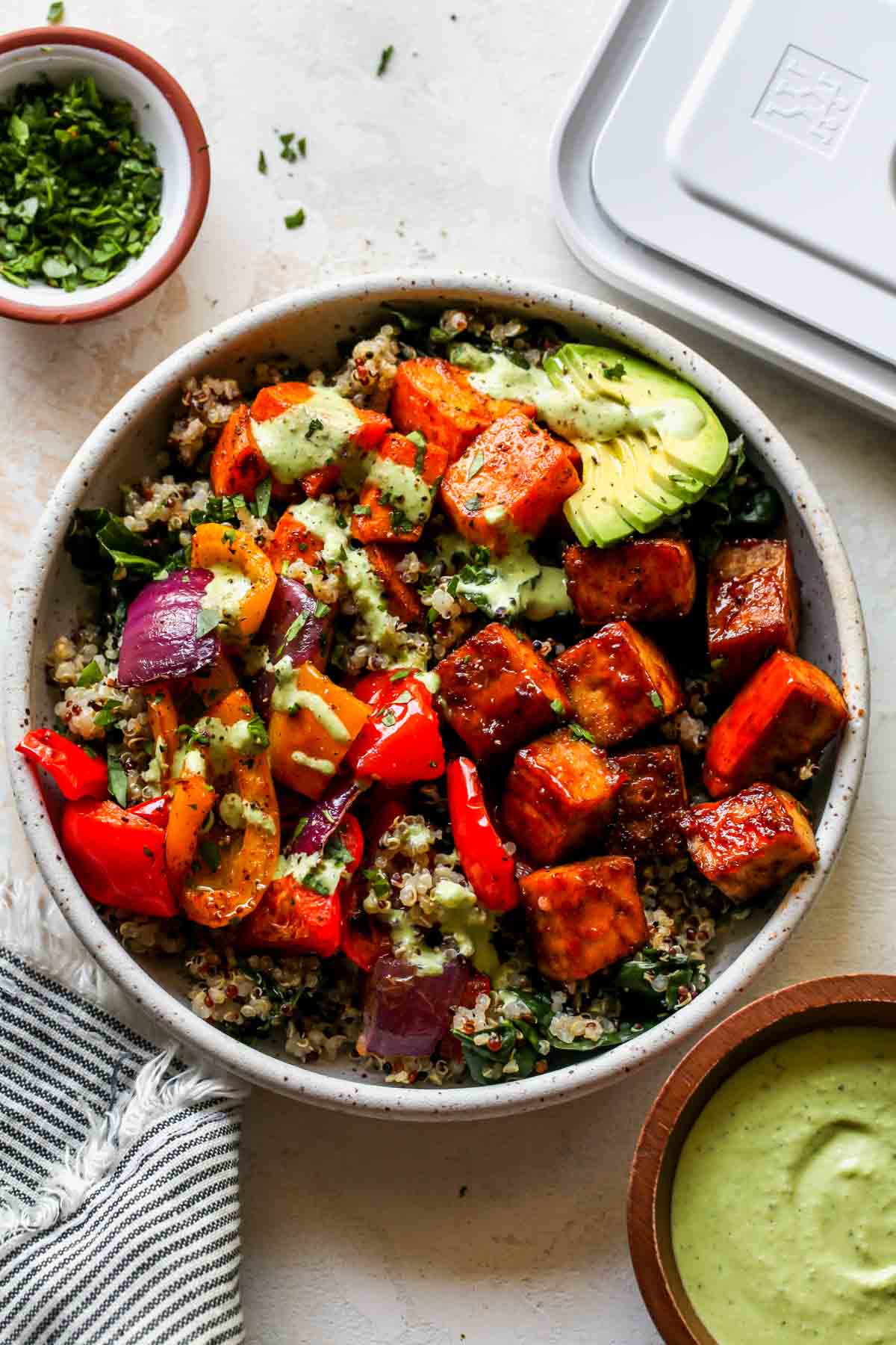 BBQ tofu, sweet potato, peppers and onions in a white bowl topped with jalapeño ranch sauce