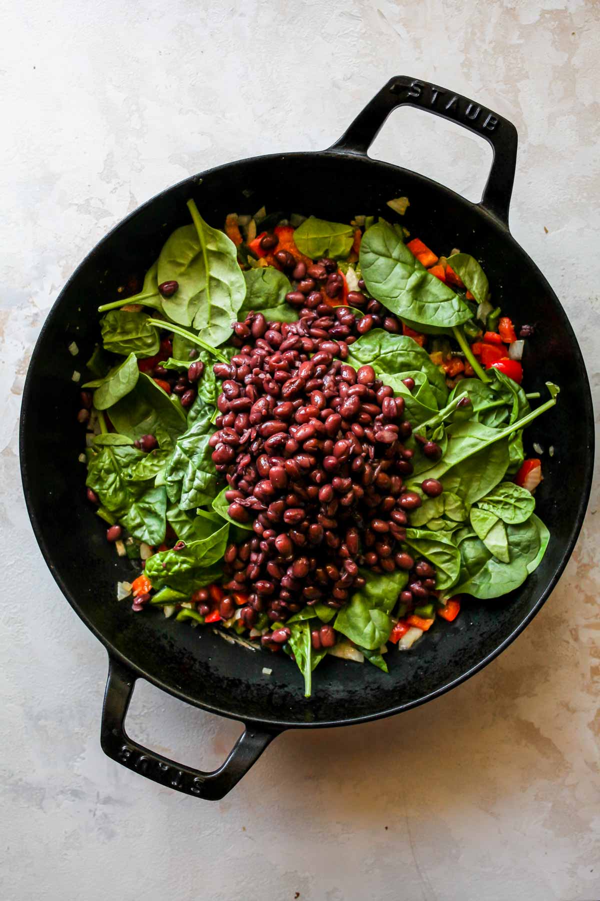 Spinach and black beans being stirred into a mix of onion and peppers