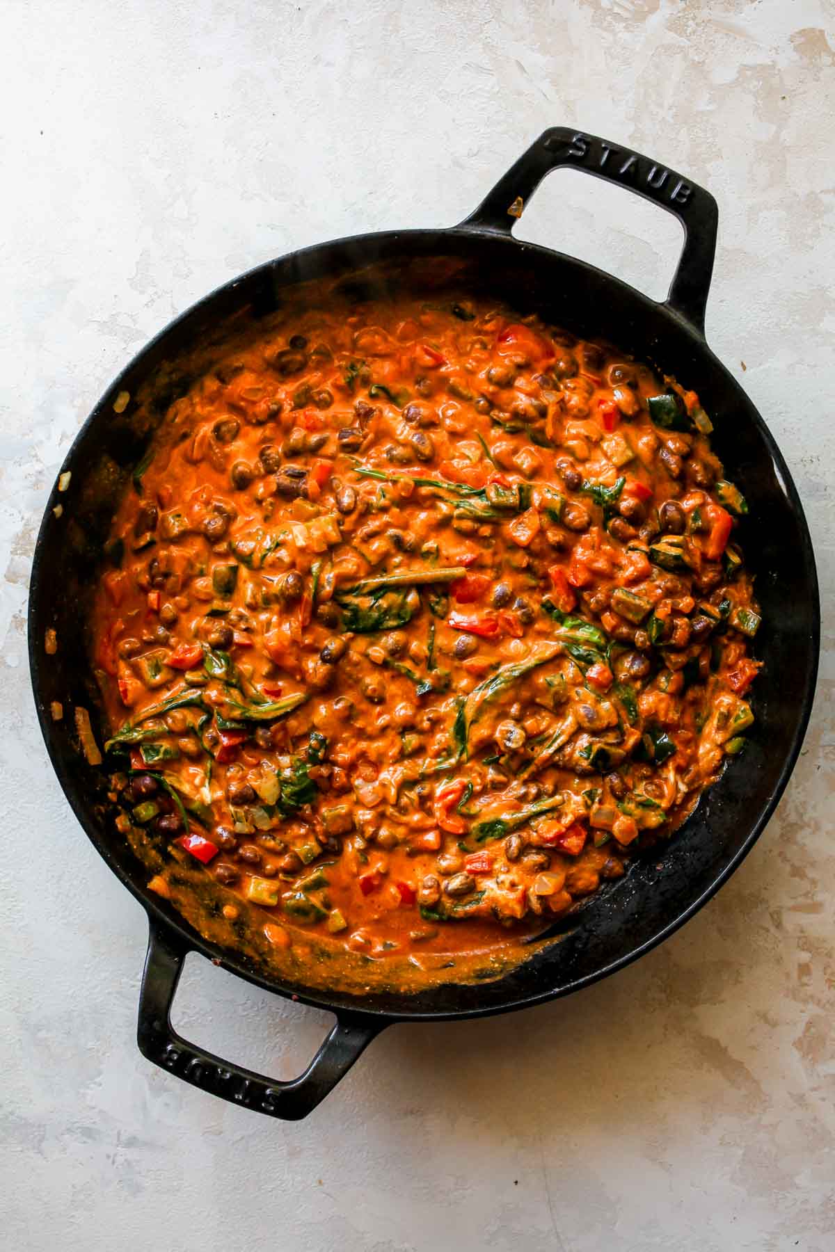Enchilada sauce, sour cream, and pumpkin puree being stirred into a skillet