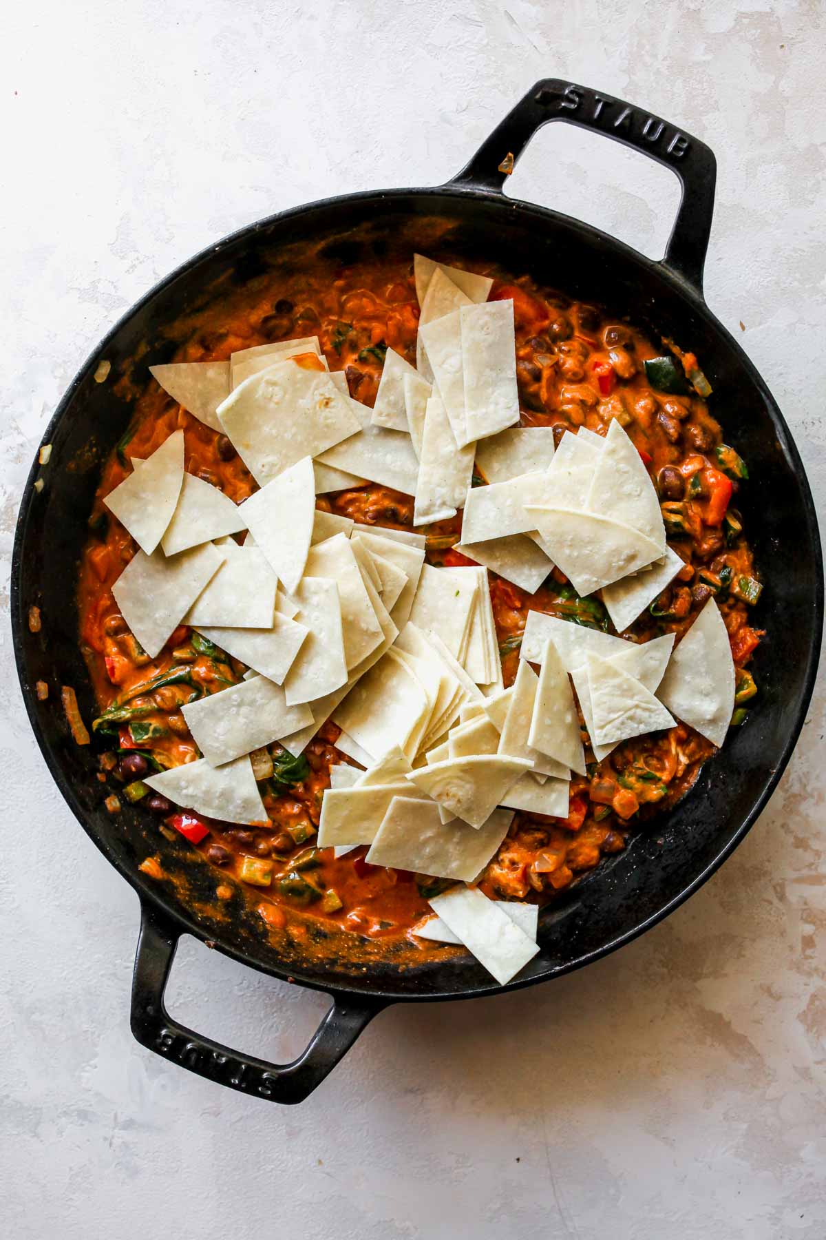 Chopped tortilla strips being stirred in a pan of enchilada sauce