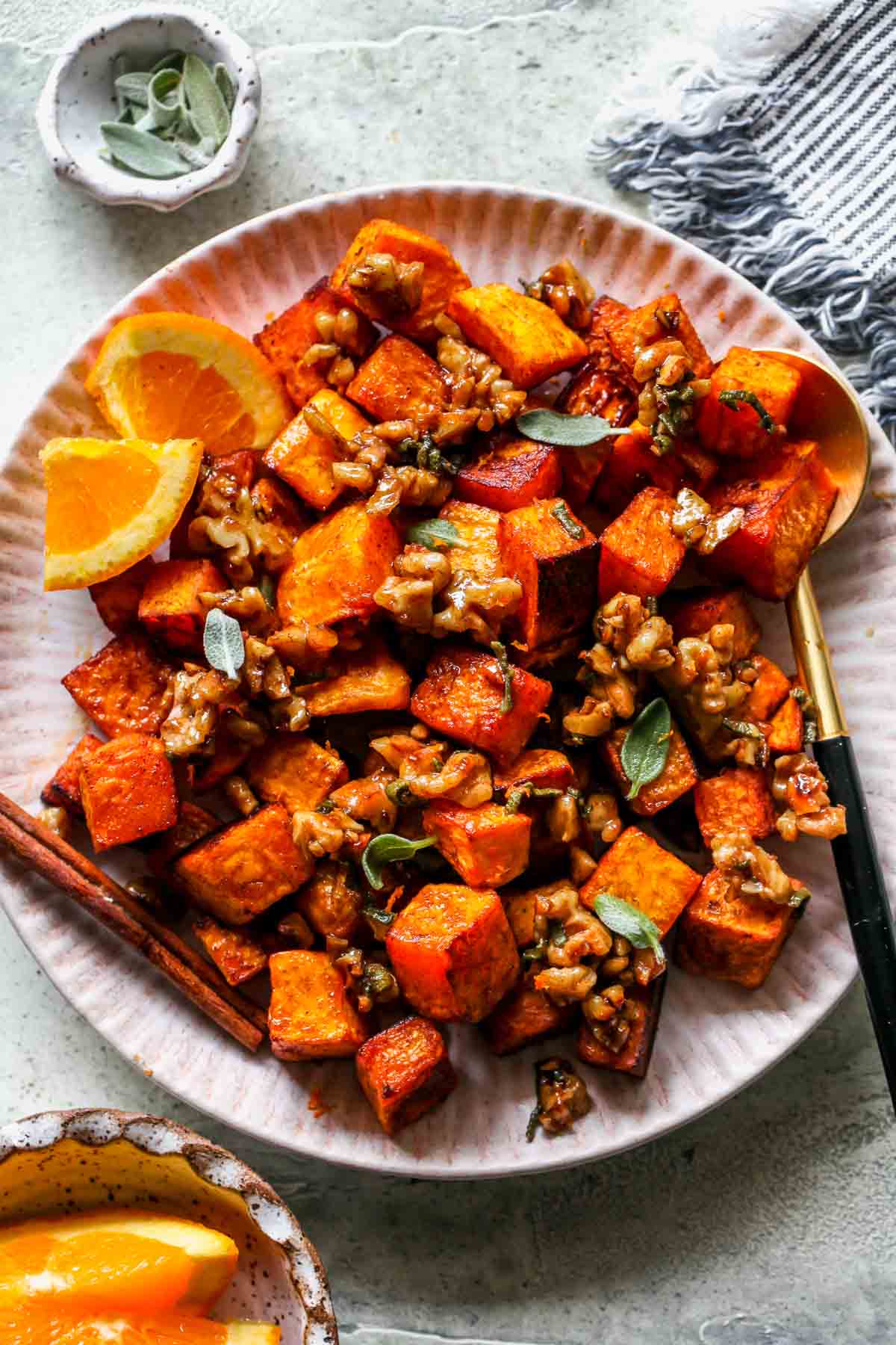 Roasted butternut squash topped with candied walnuts assembled on a pink scalloped plate.