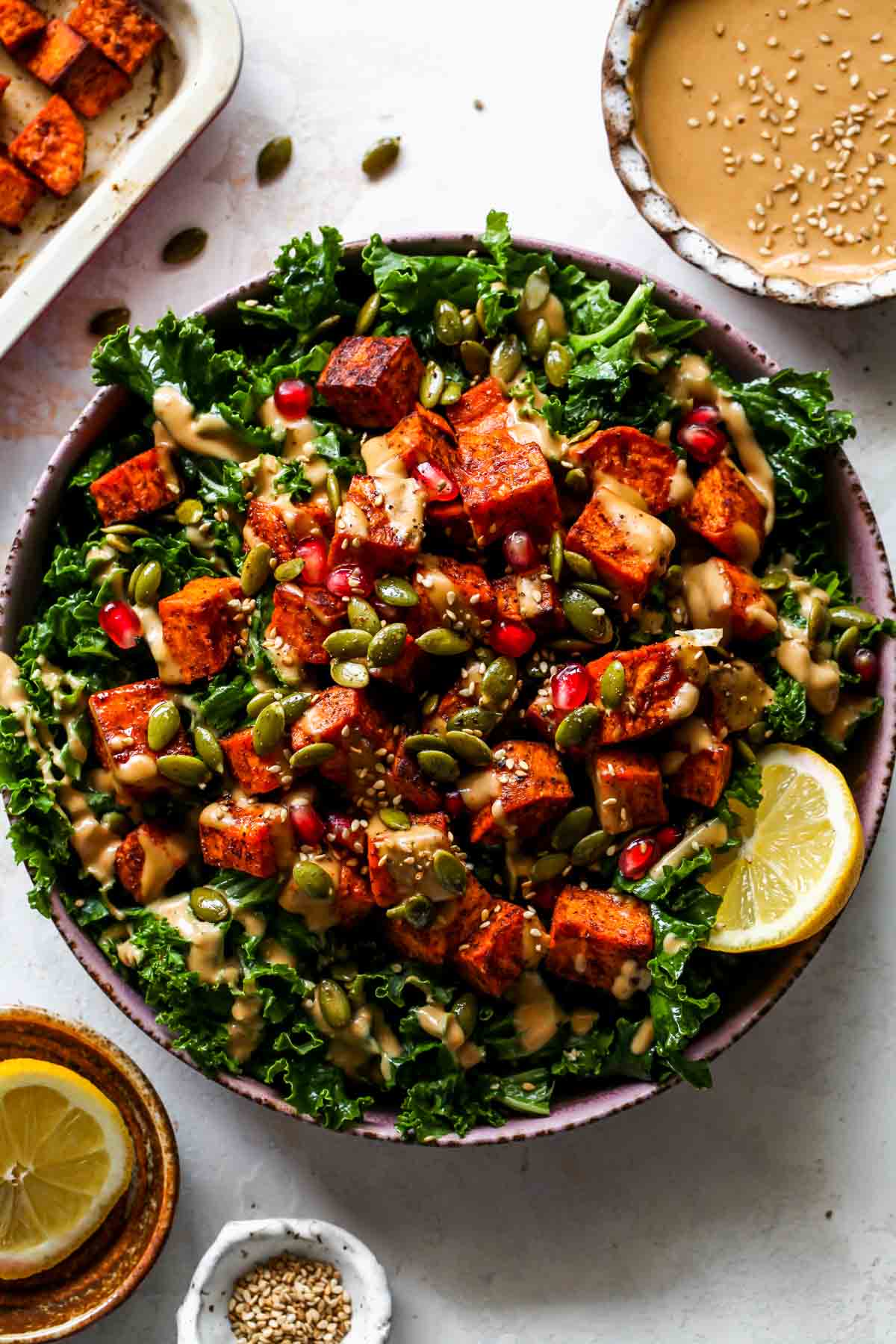 Kale salad topped with roasted sweet potatoes, pomegranate, and almond butter dressing