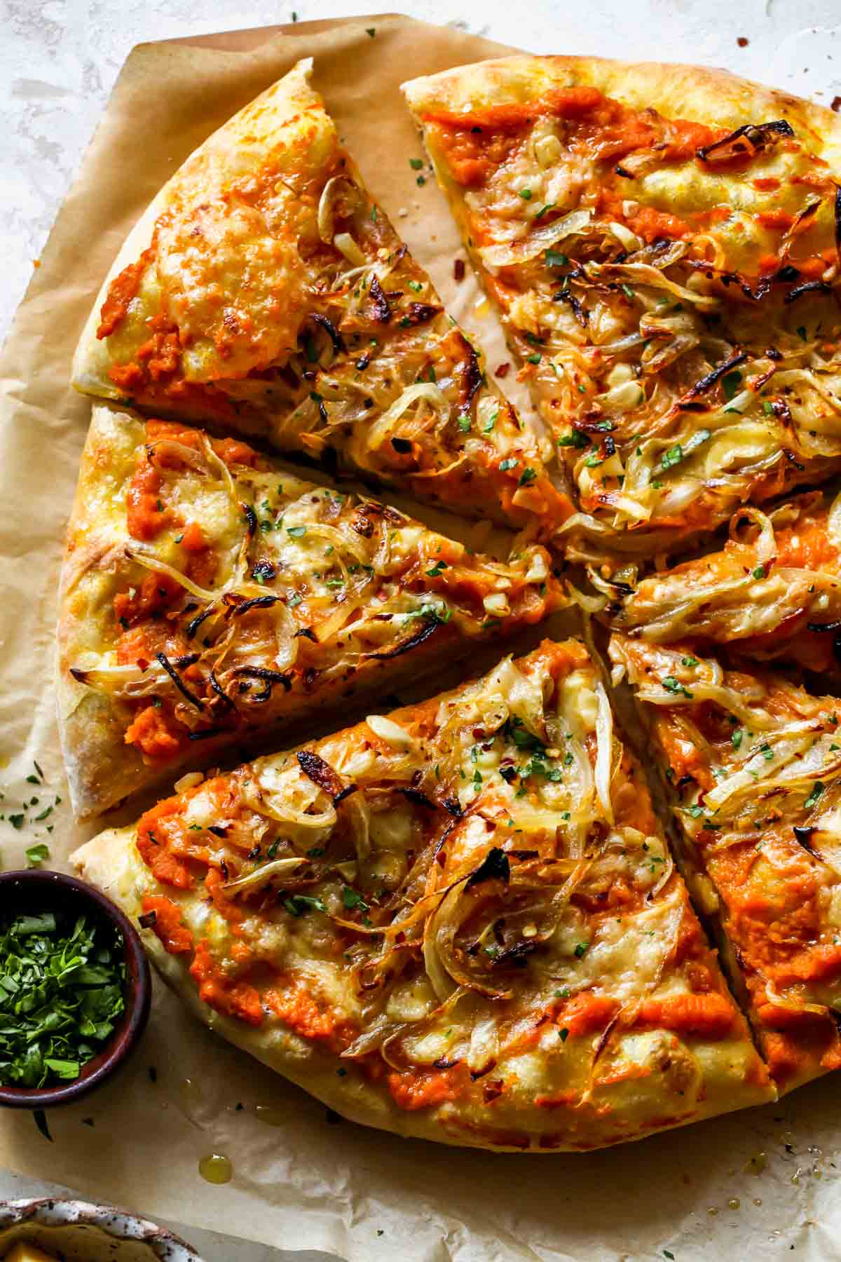 Pumpkin and gouda pizza being sliced on a piece of parchment paper