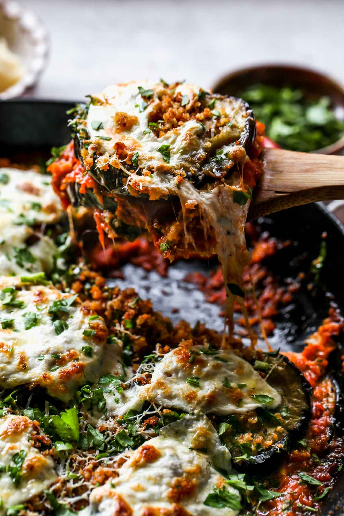 A piece of eggplant parm being pulled out of skillet to show cheese pull