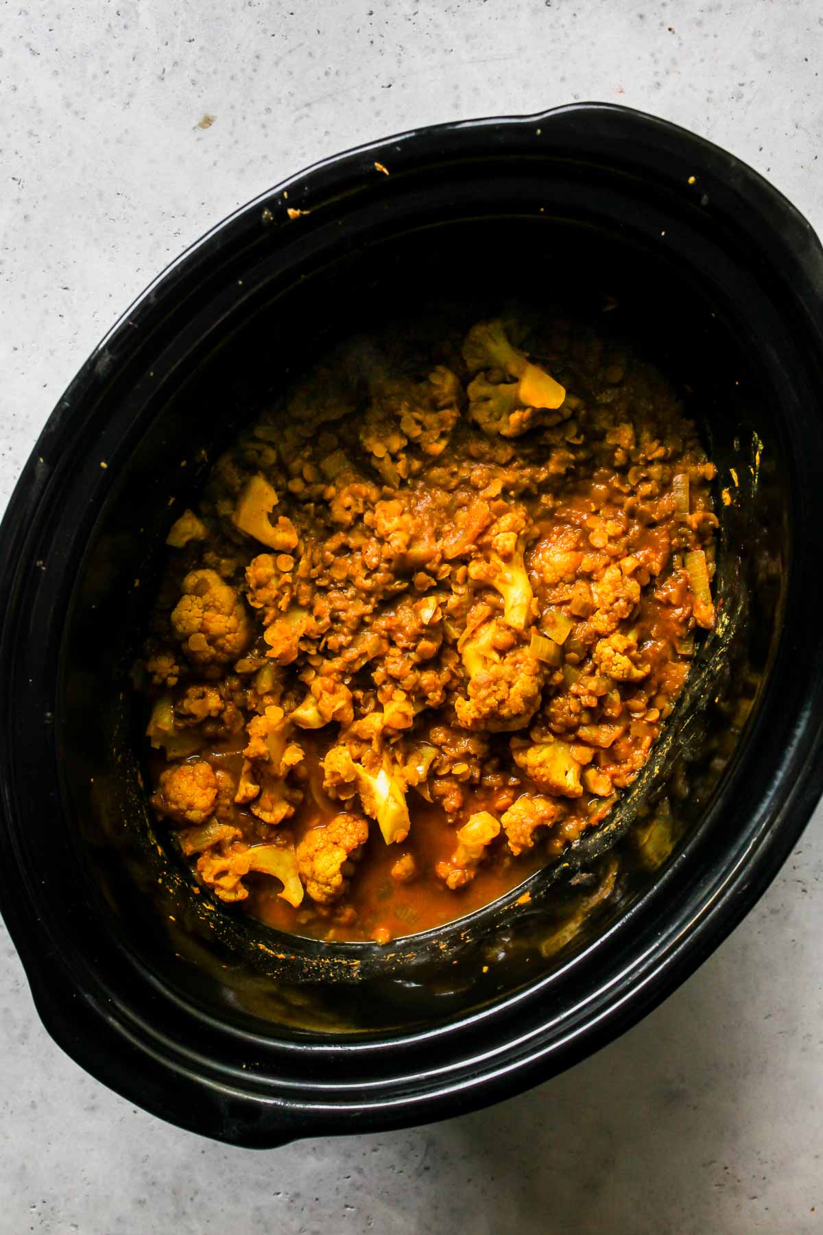 Cauliflower, lentils, spices, and coconut milk in a black slow cooker