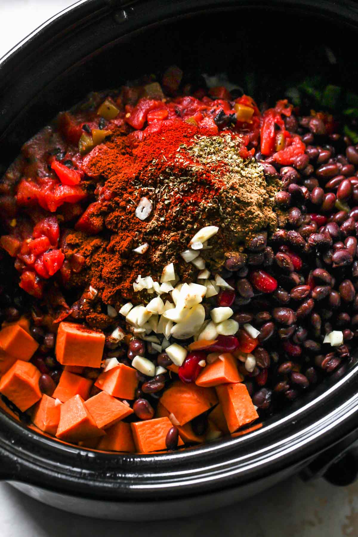 Sweet potato, beans, tomatoes, and spices being added to a slow cooker
