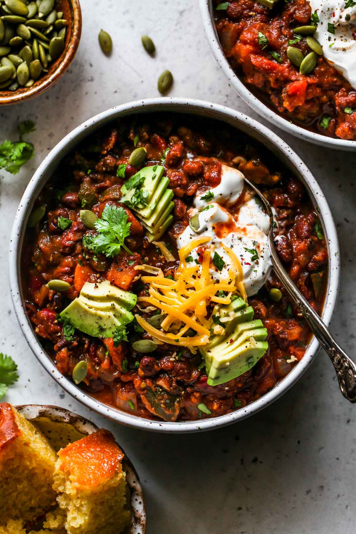 Sweet potato black bean chili in a white bowl topped with avocado, sour cream, and cheese