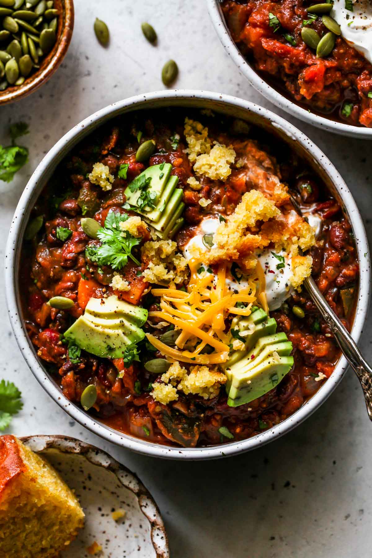 A spoon digging into a bowl of crockpot chili topped with cornbread